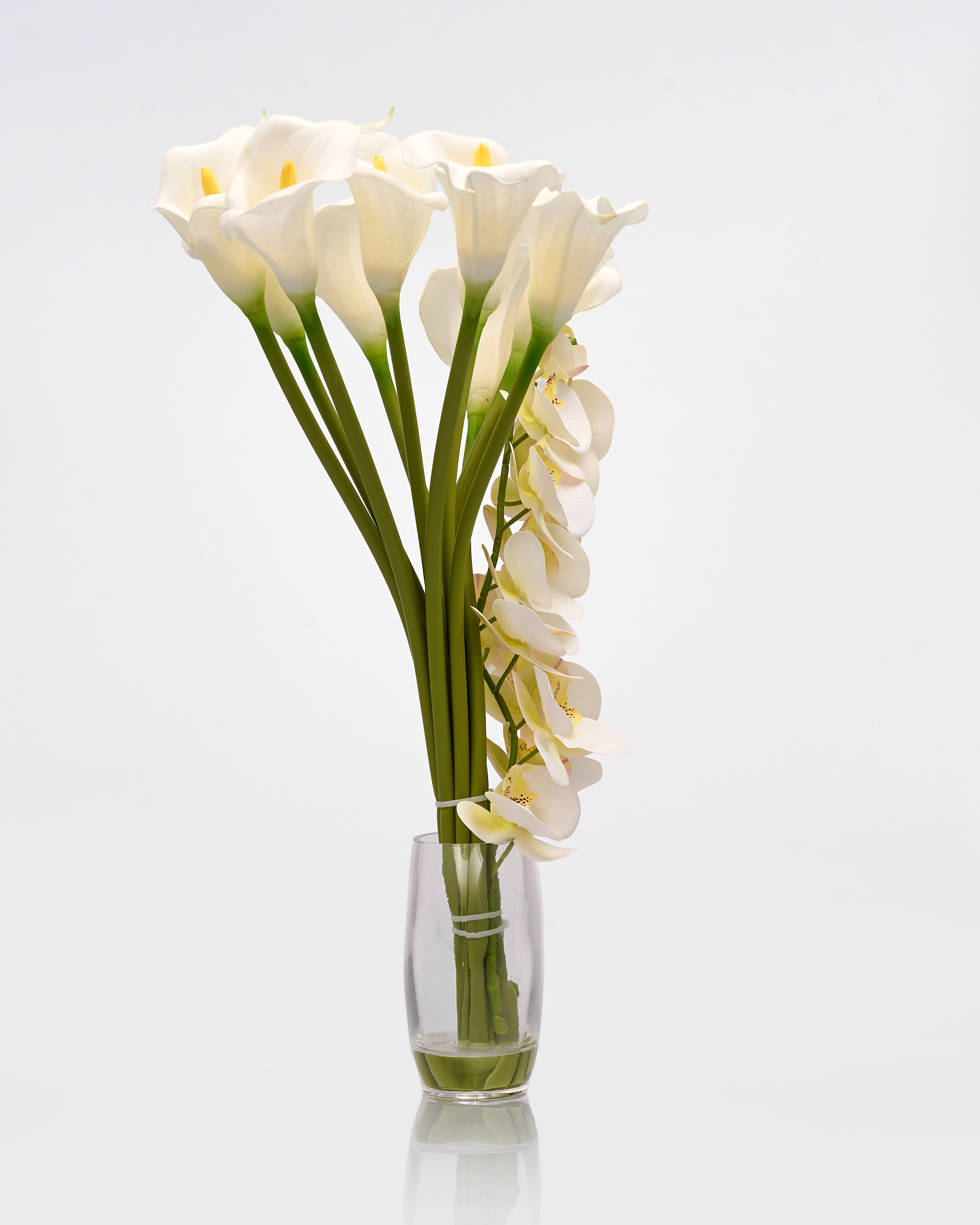 Bouquet of white calla lilies artificial in a clear glass vase on a light gray background