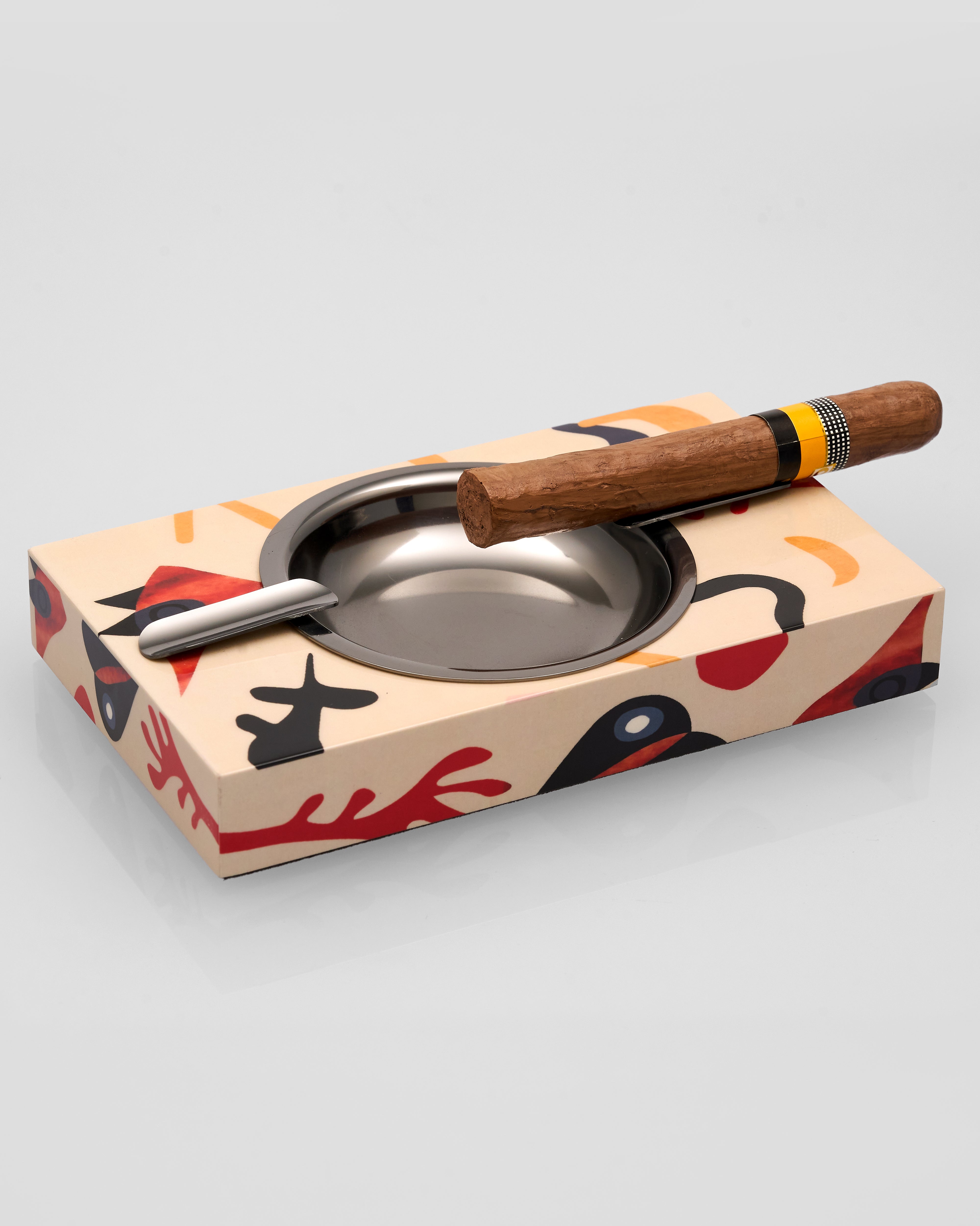 Cigar ashtray with a wooden handle on a colorful box against a light gray background
