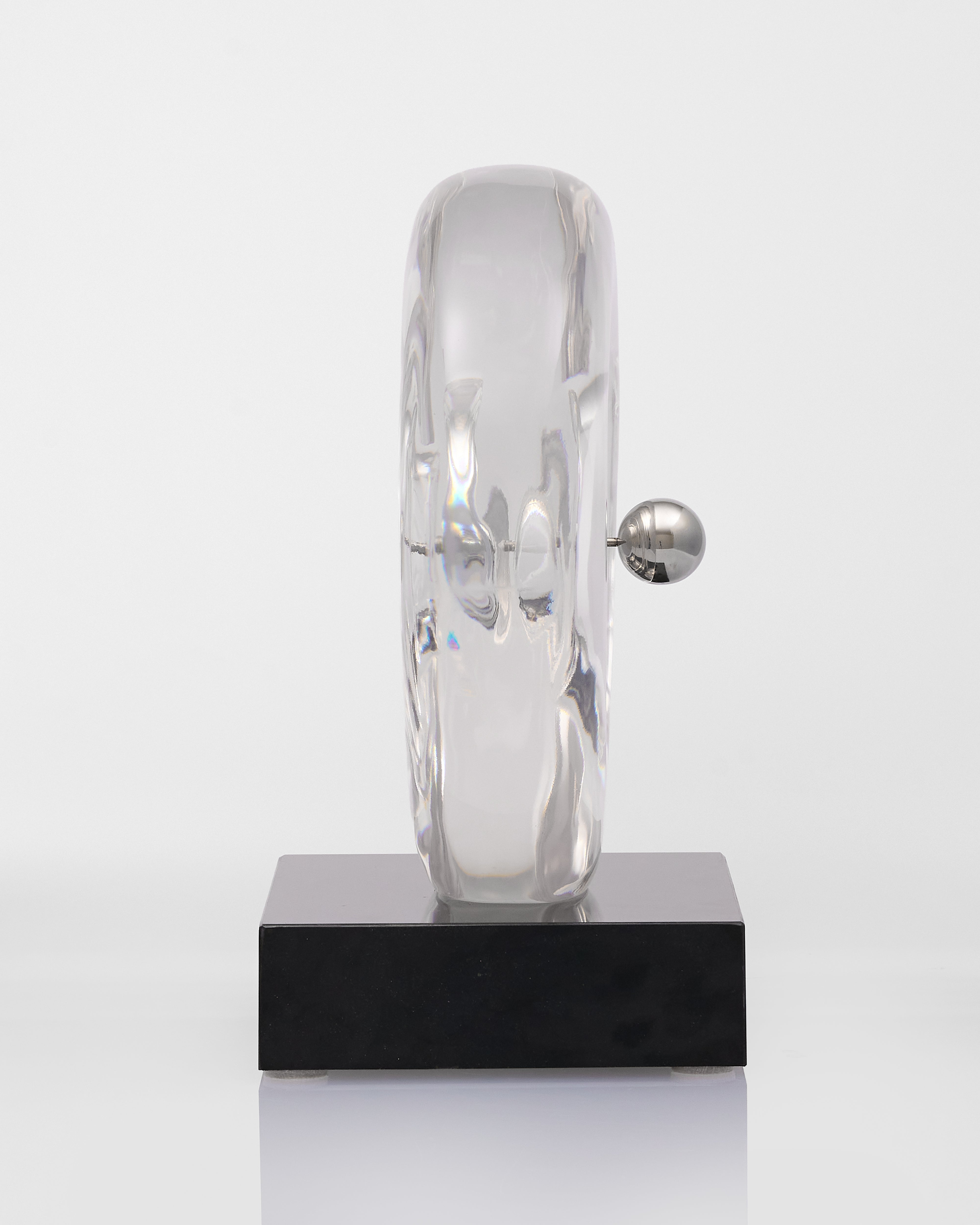 Modern sculpture with a reflective surface on a black base against a white background