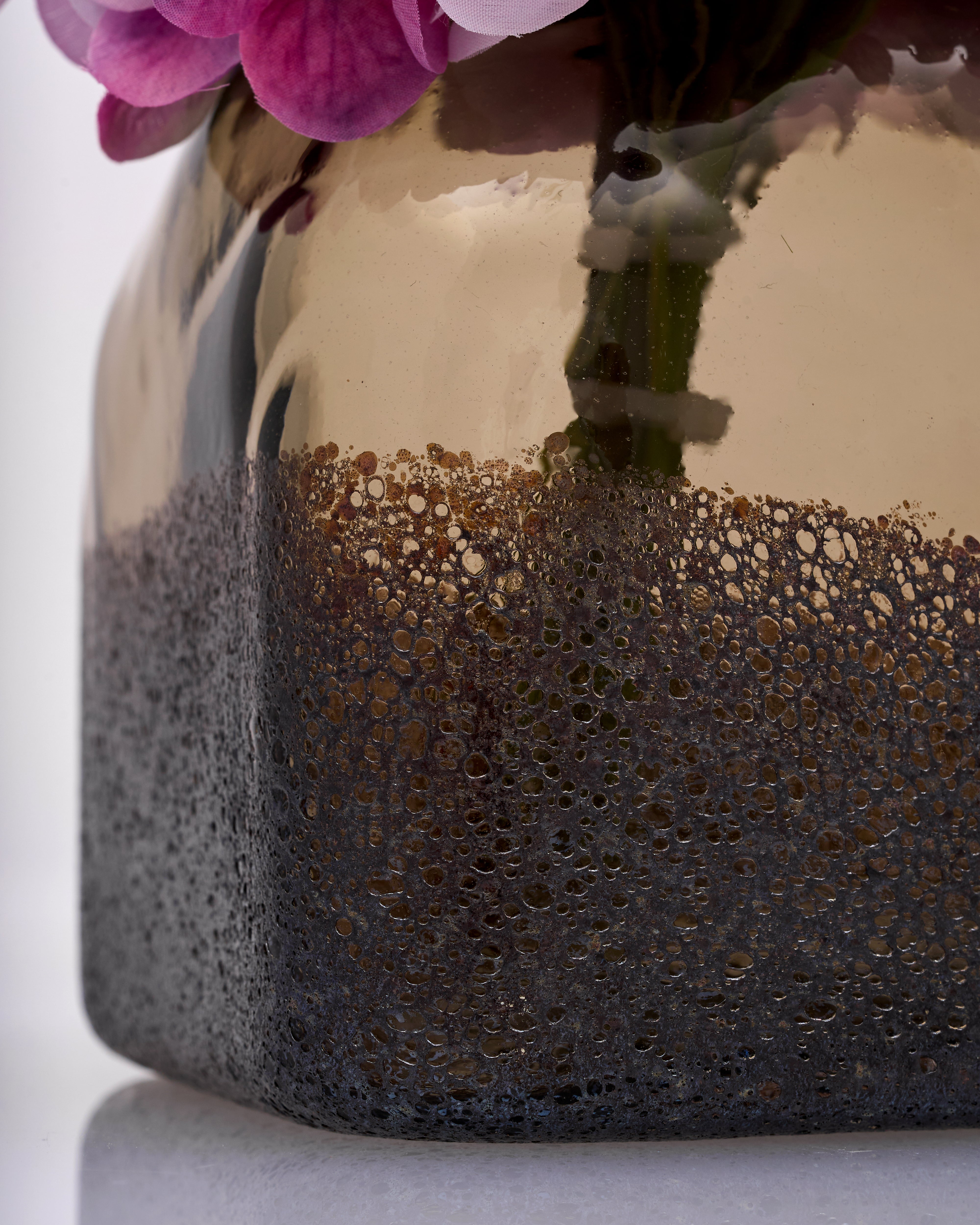 Vase with textured bottom and reflective surface, containing pink flowers.