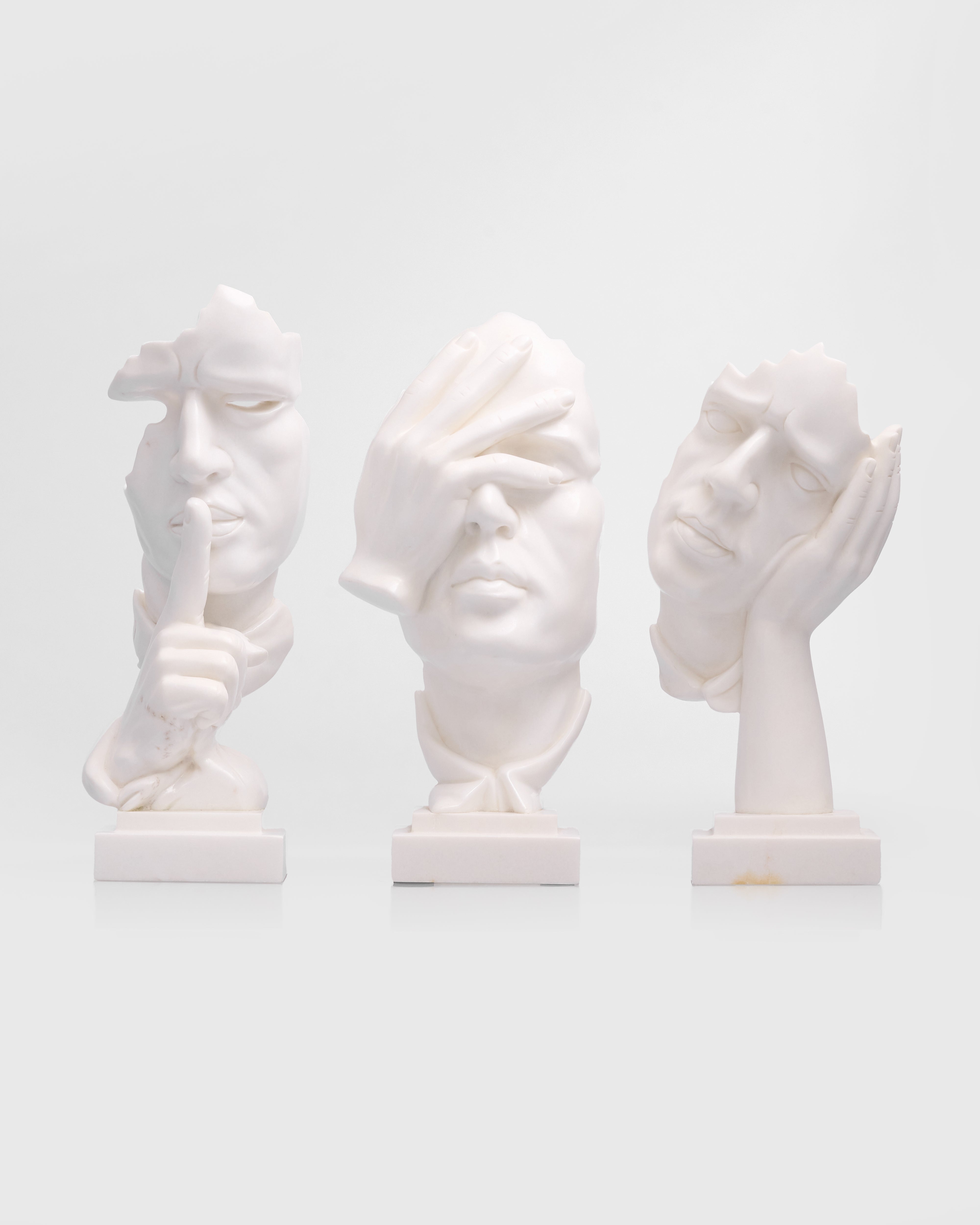 Three white marble busts of faces on a light gray background
