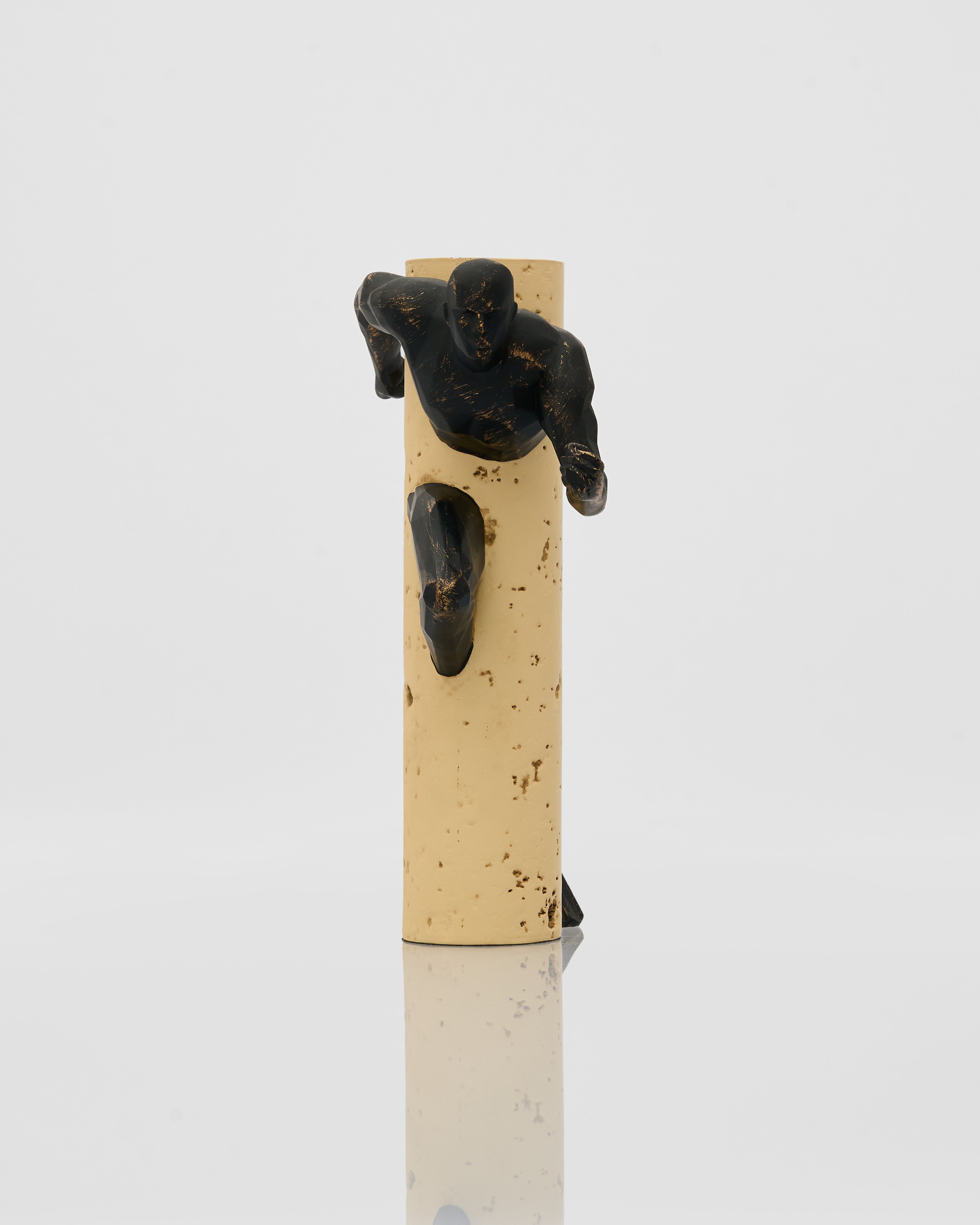 Small black sculpture of a person on a beige cylindrical block against a white background
