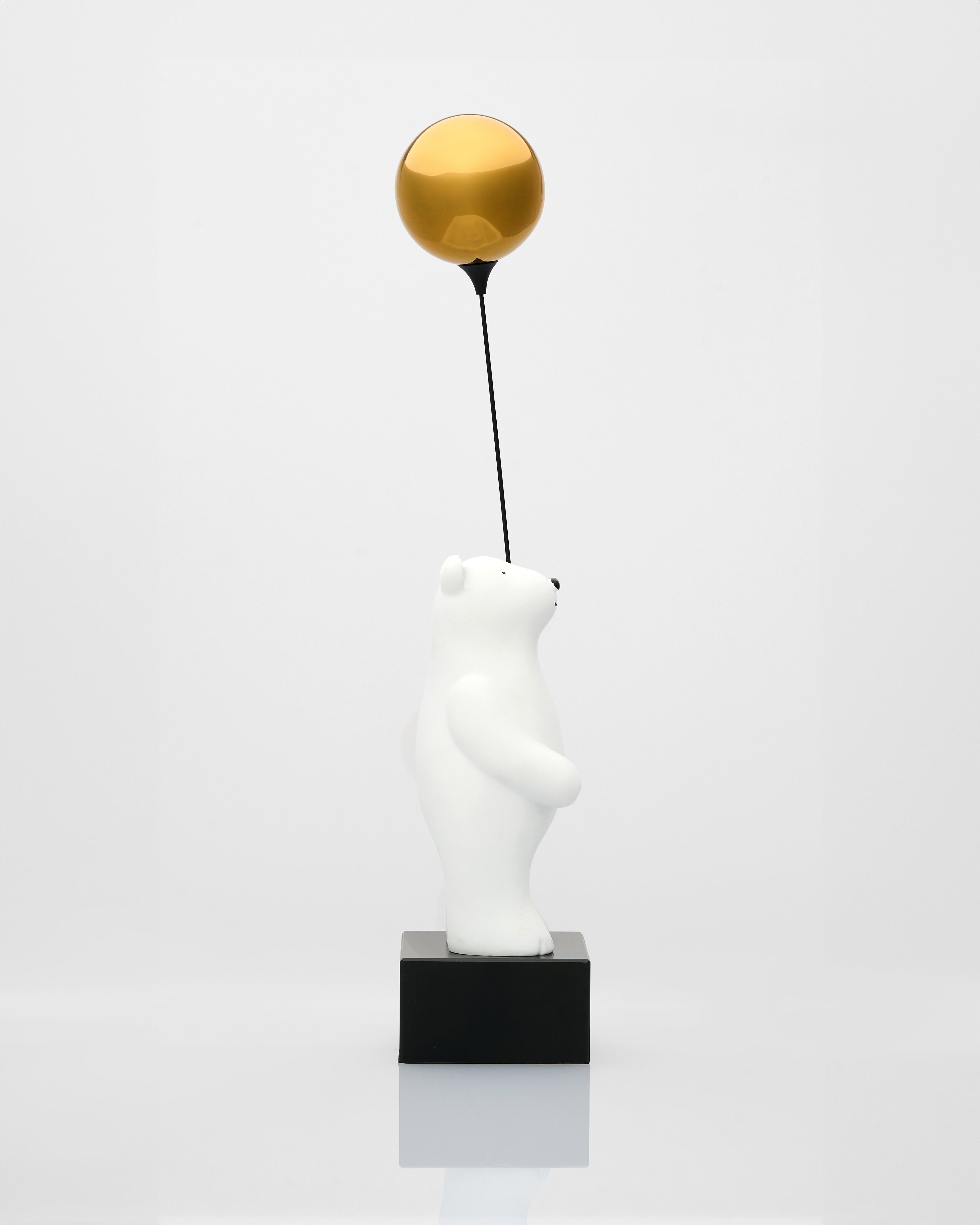 White polar bear figurine holding a gold ball on a black stand against a white background