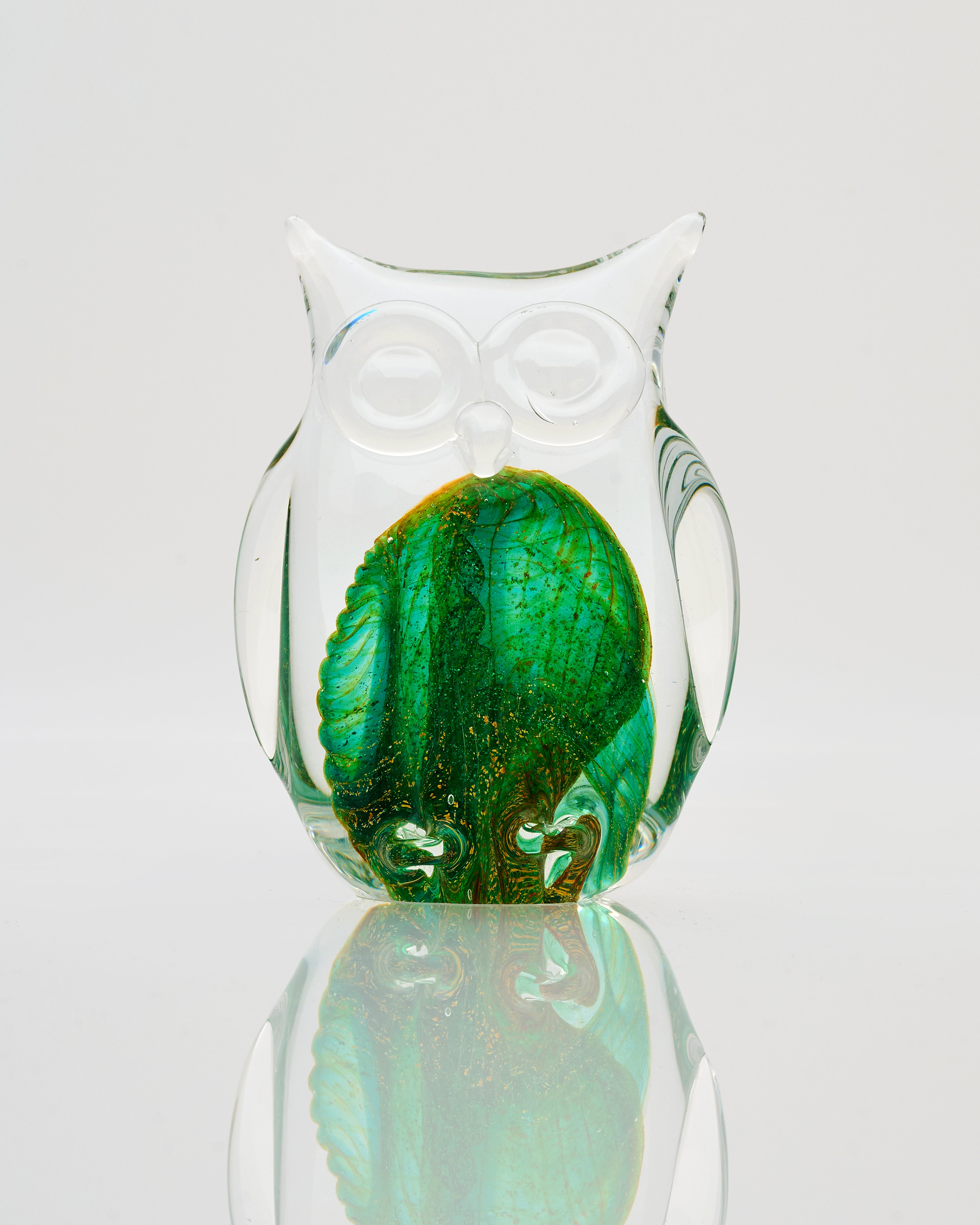 Glass owl with green interior on a reflective surface