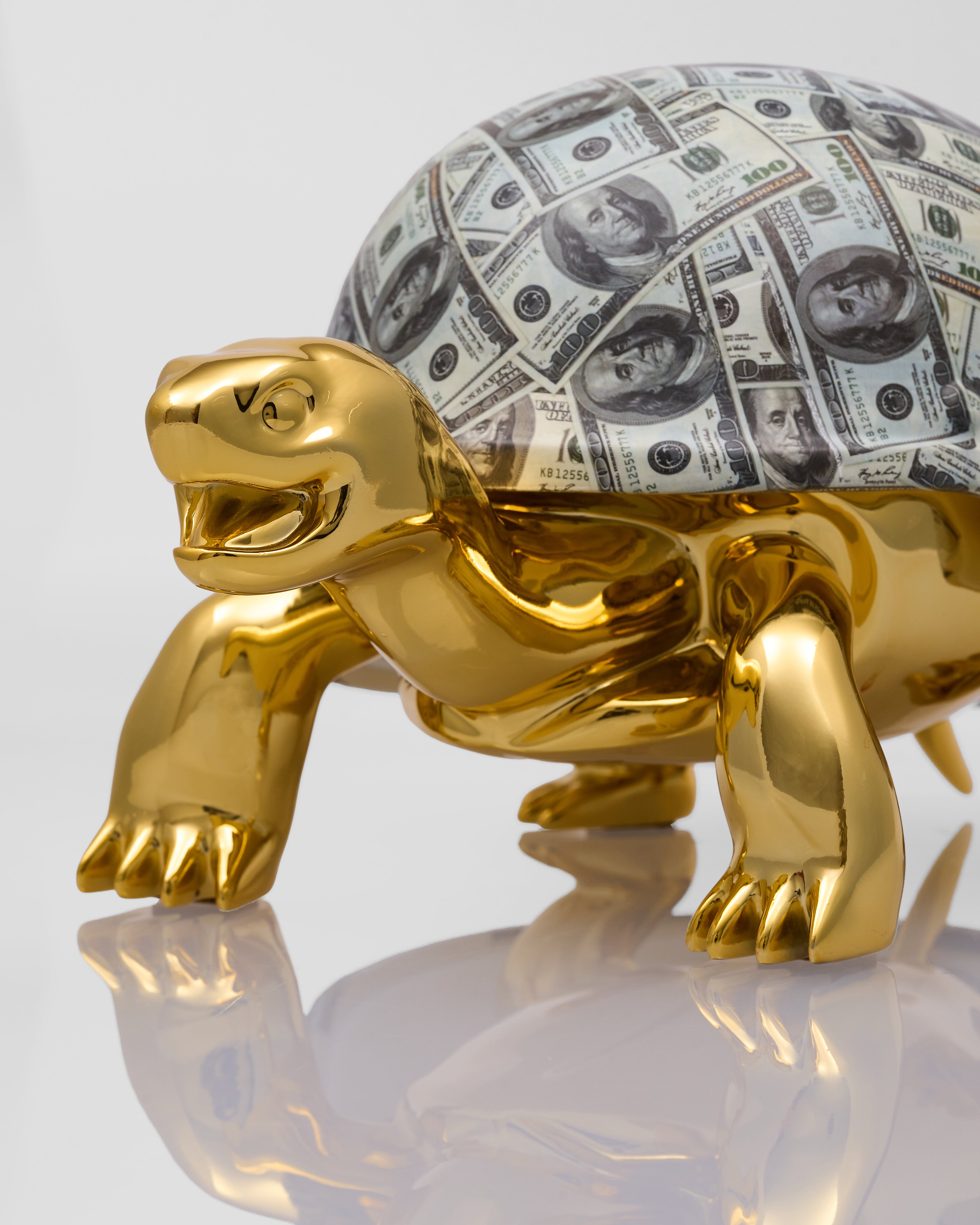 Gold turtle figurine with a shell made of dollar bills on a white background