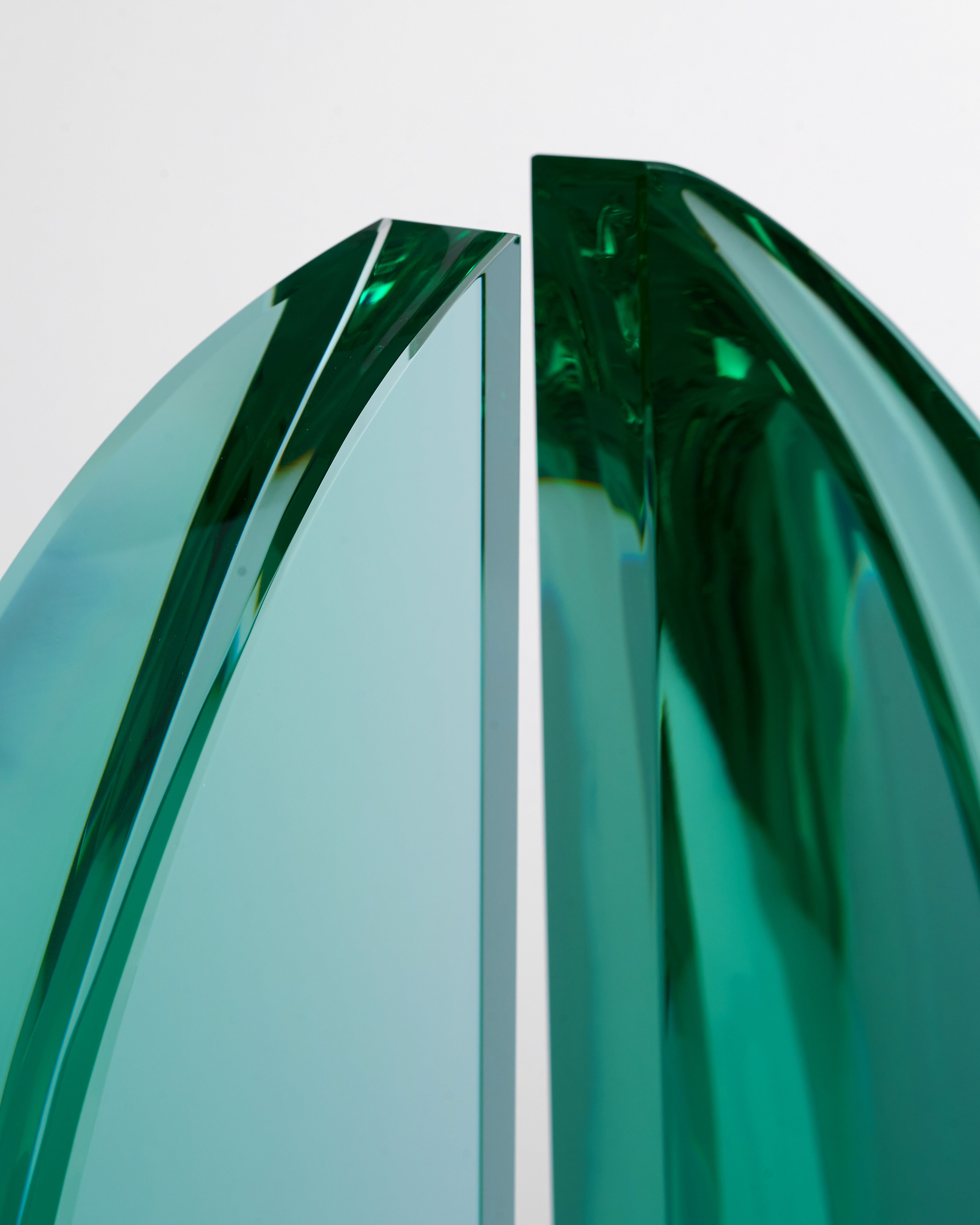 Close-up of a green glass object with a reflective surface on a light gray background
