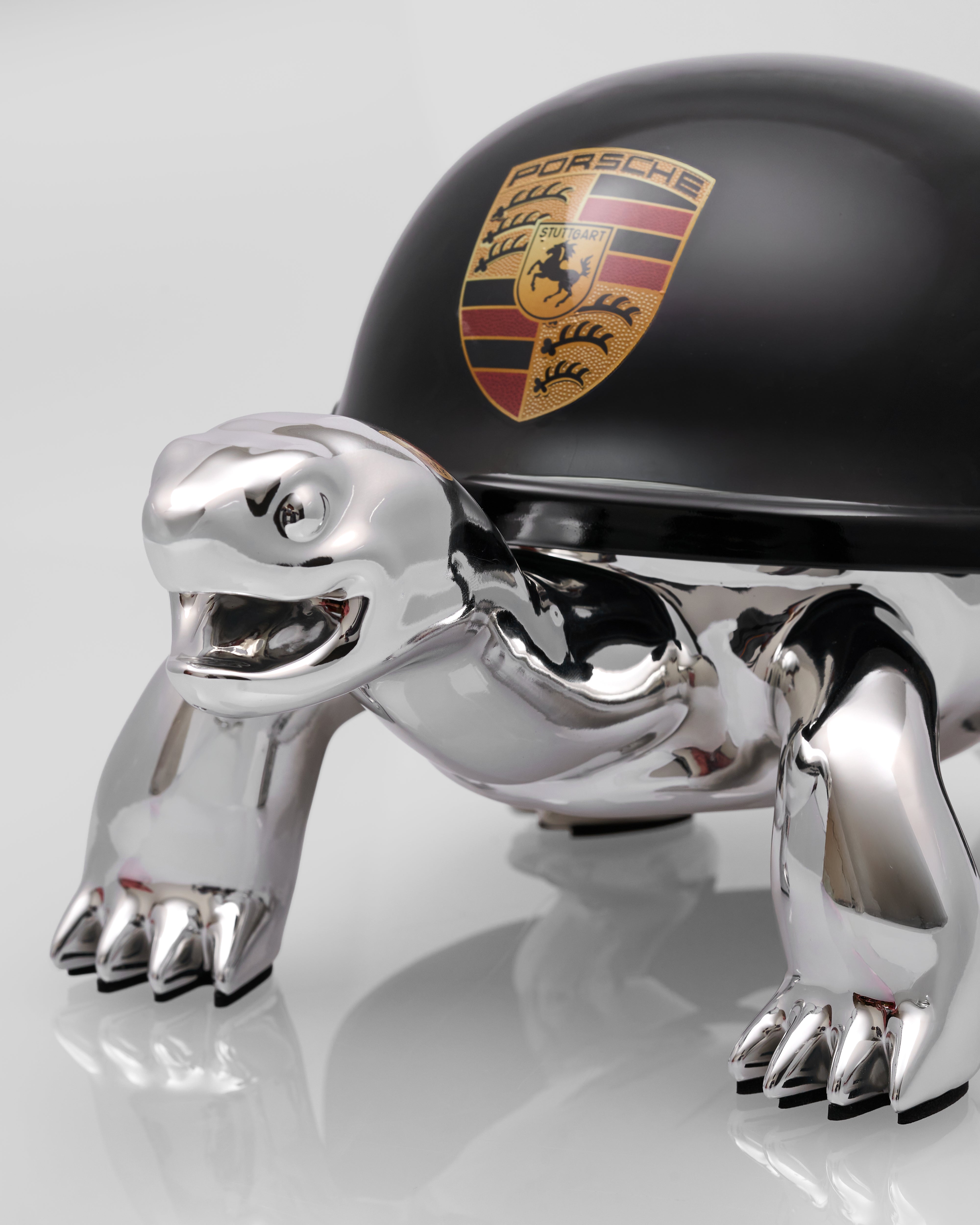 Chrome turtle-shaped car mascot with Porsche logo on a white background