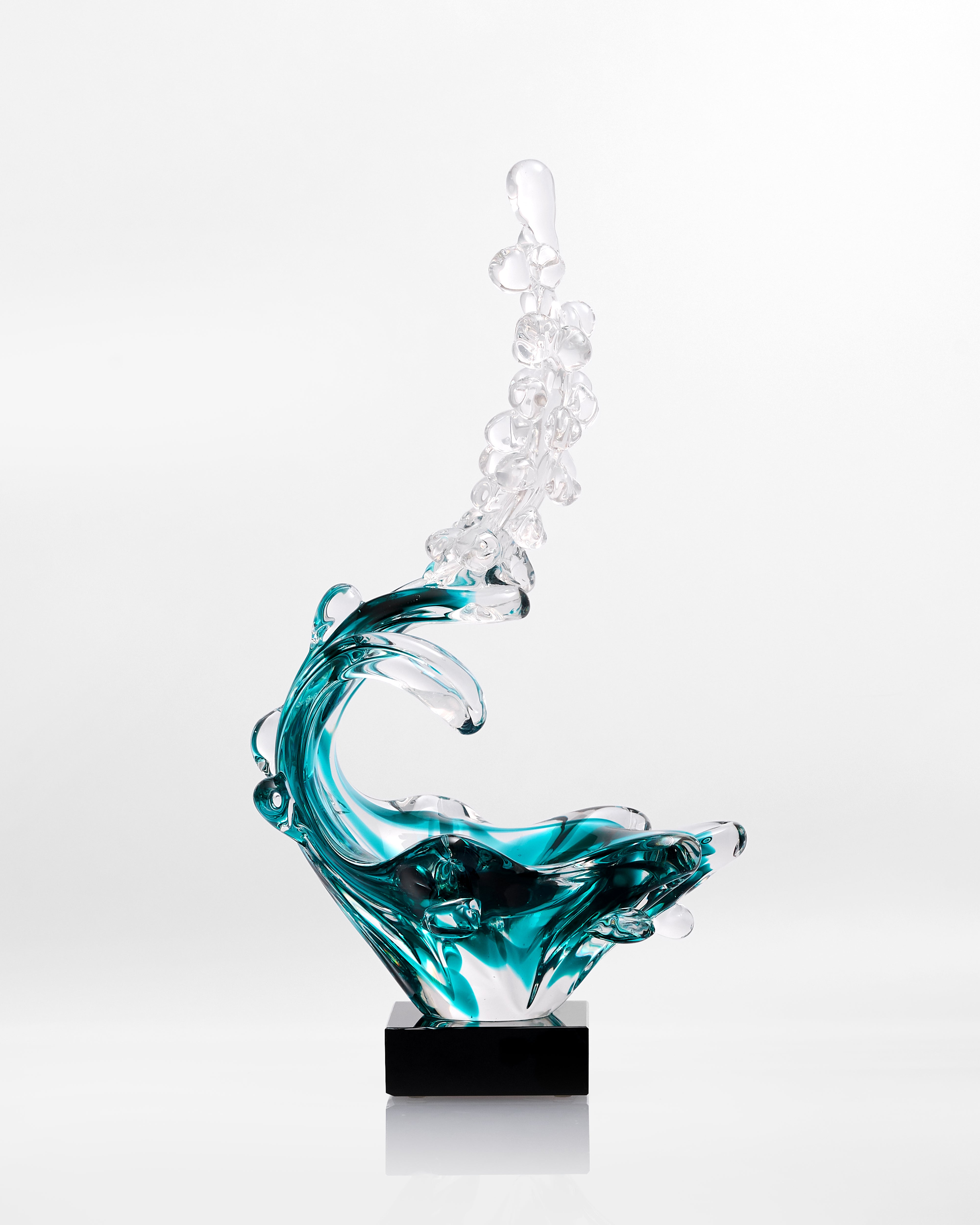 Glass sculpture of a wave with blue and clear colors on a white background