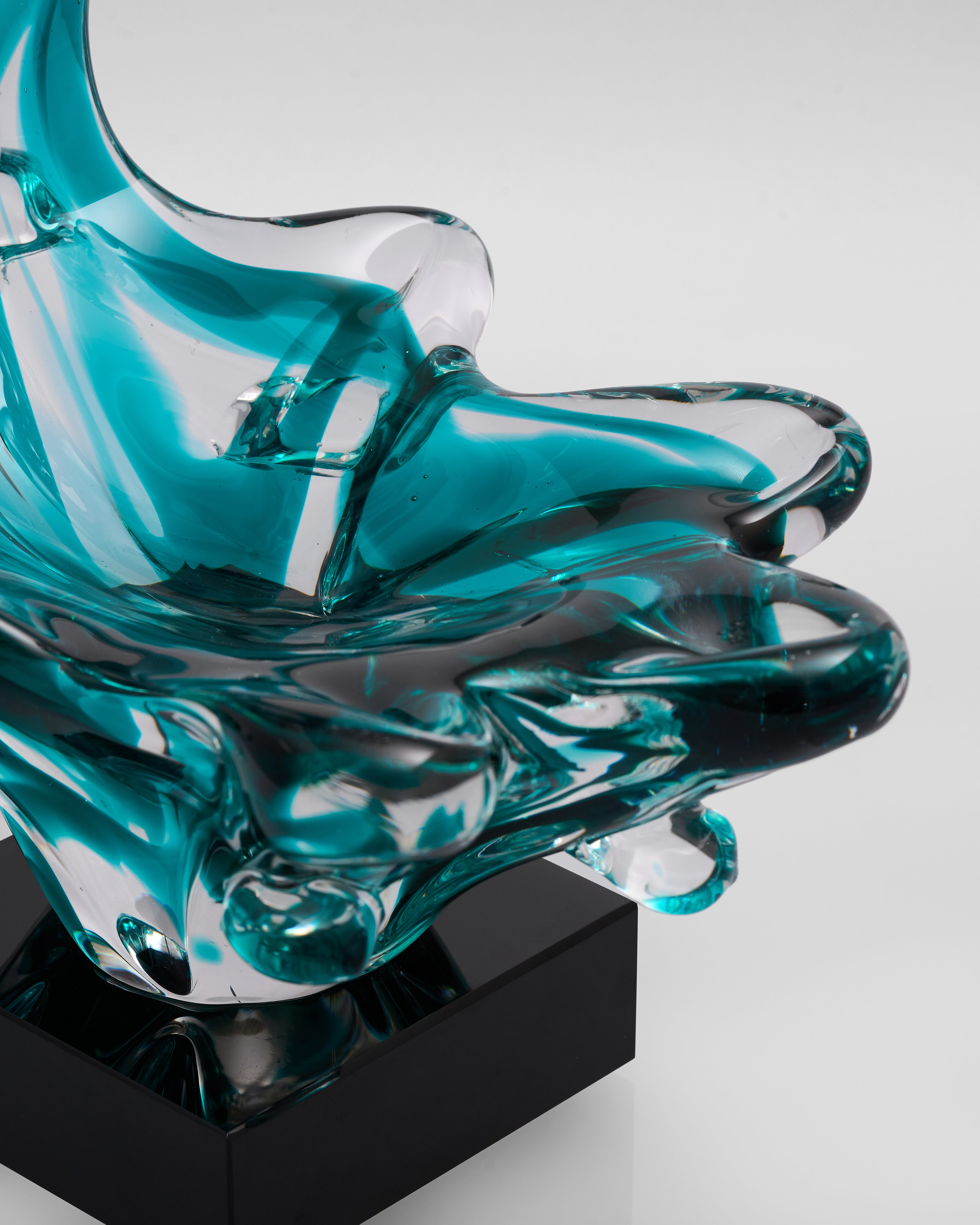 Turquoise glass sculpture on a black base against a white background