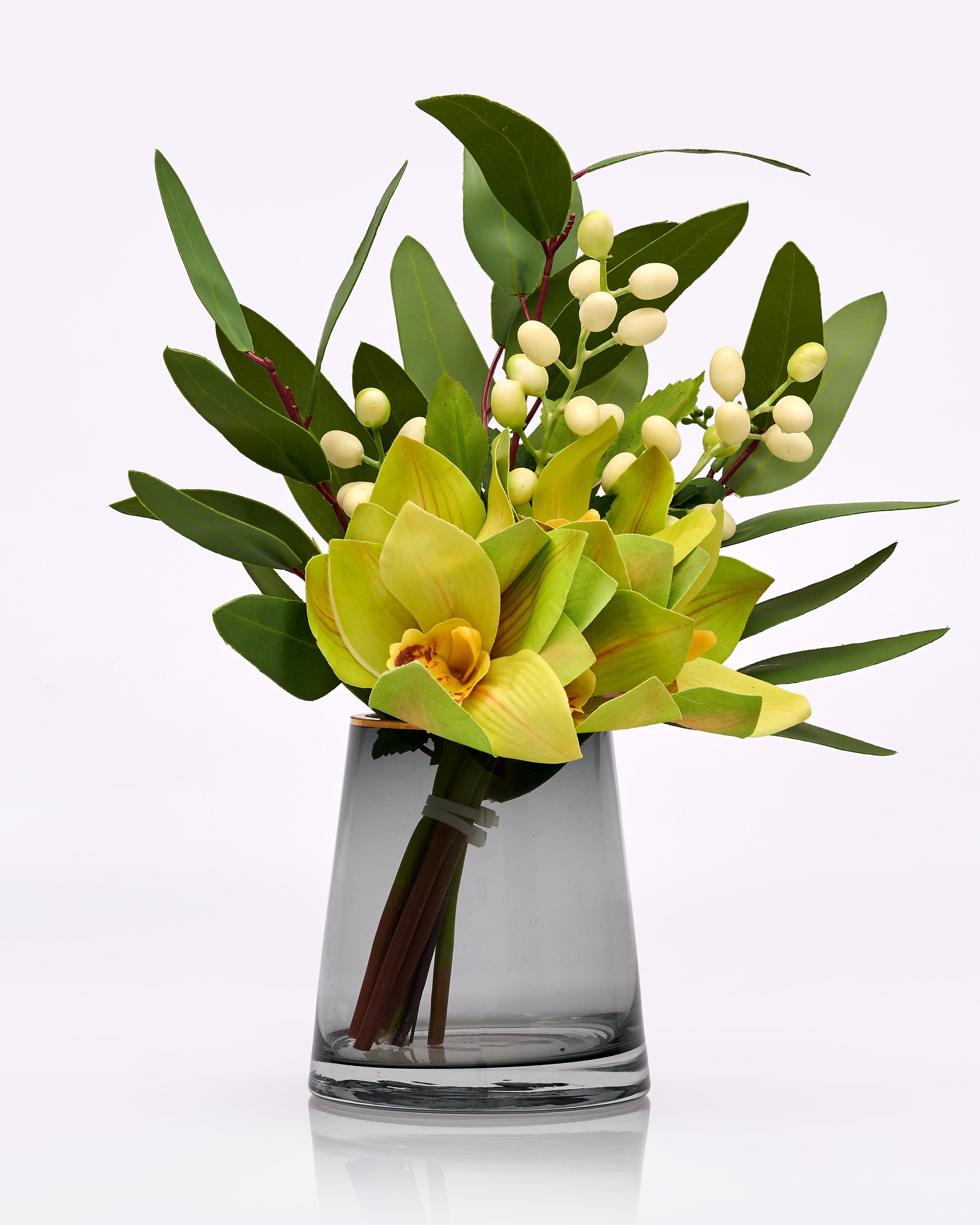 Bouquet of yellow flowers and green leaves in a clear glass vase on a white background