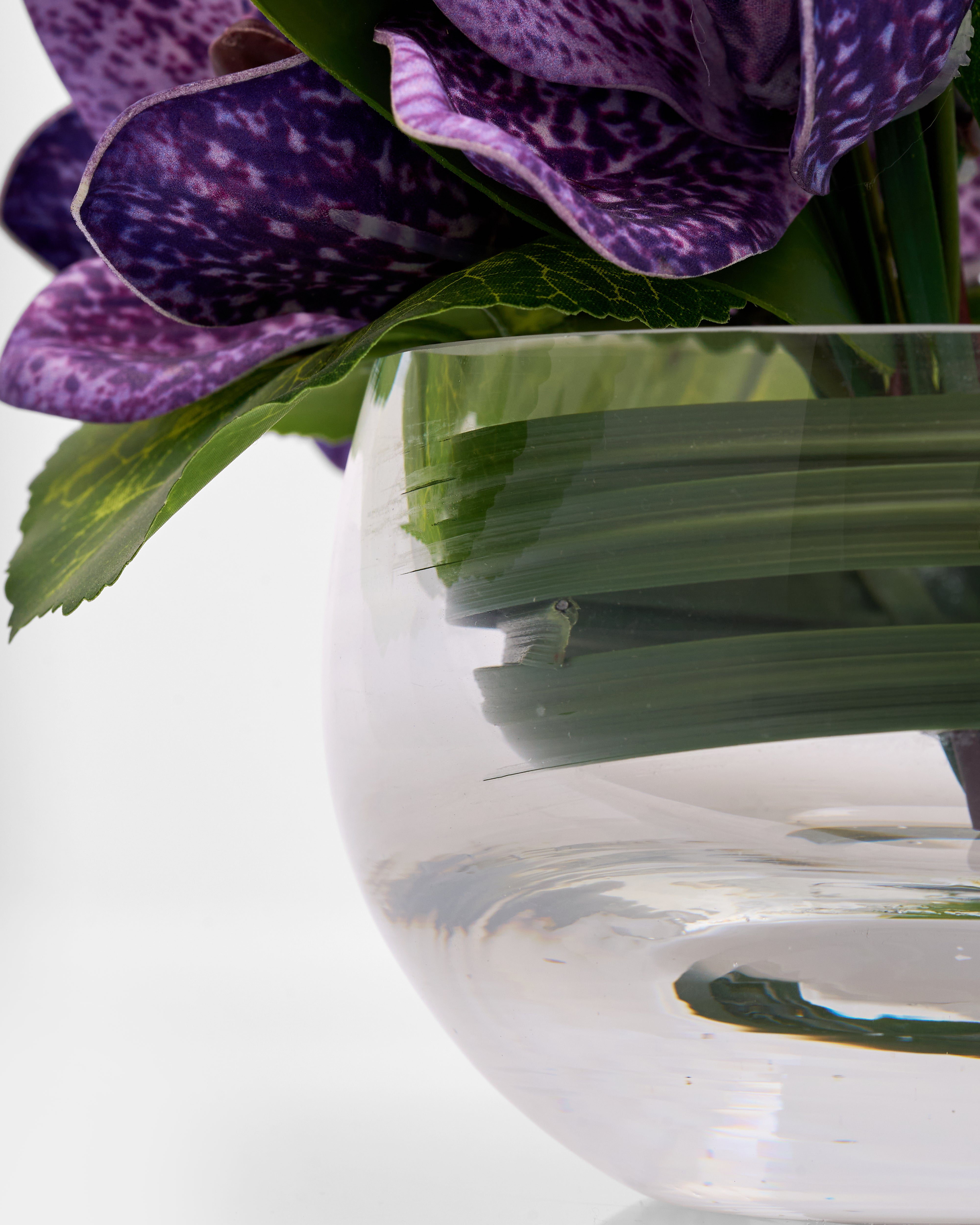 Clear glass vase with purple flowers and green leaves on a white background