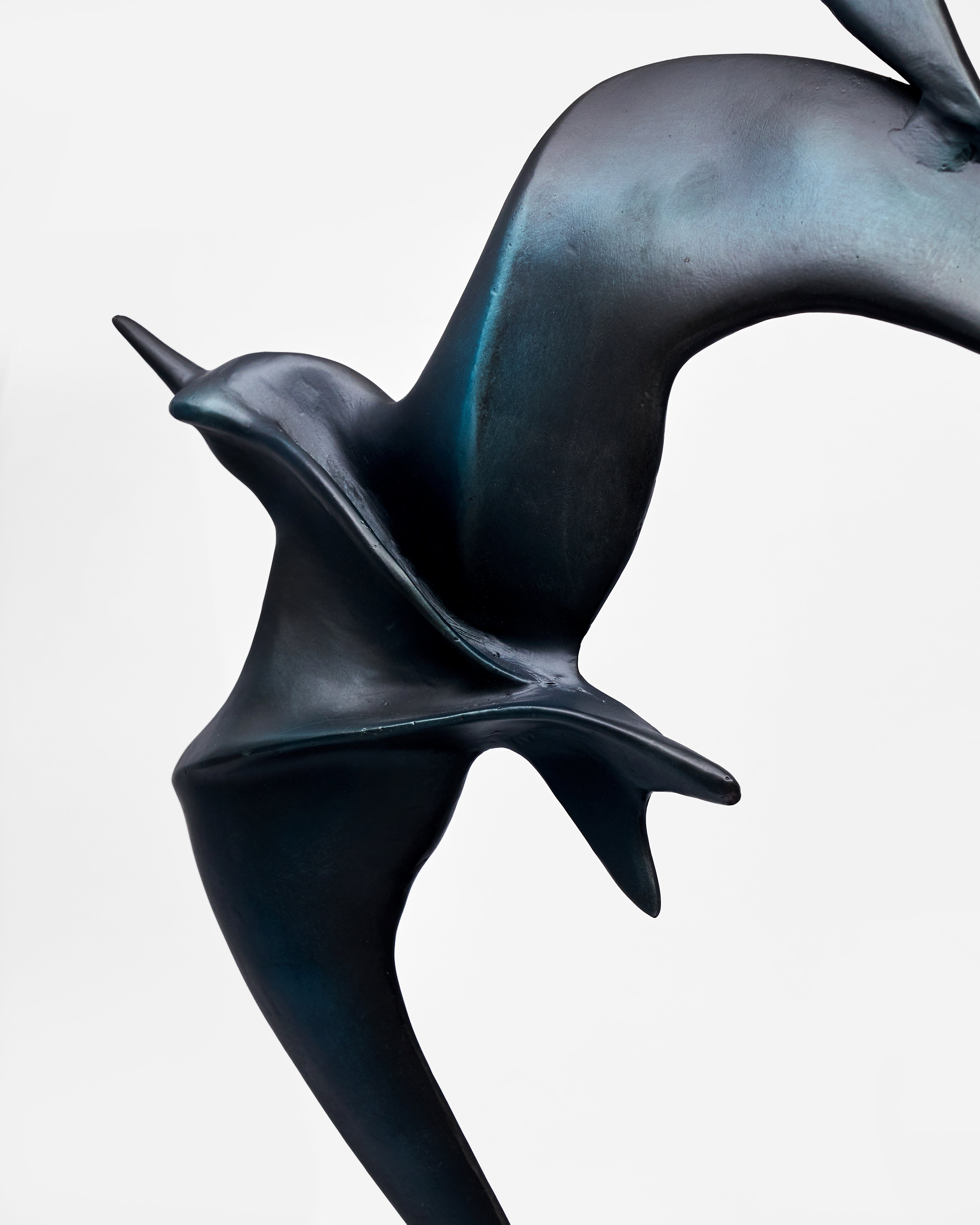 Bronze sculpture of a bird in flight on a light gray background