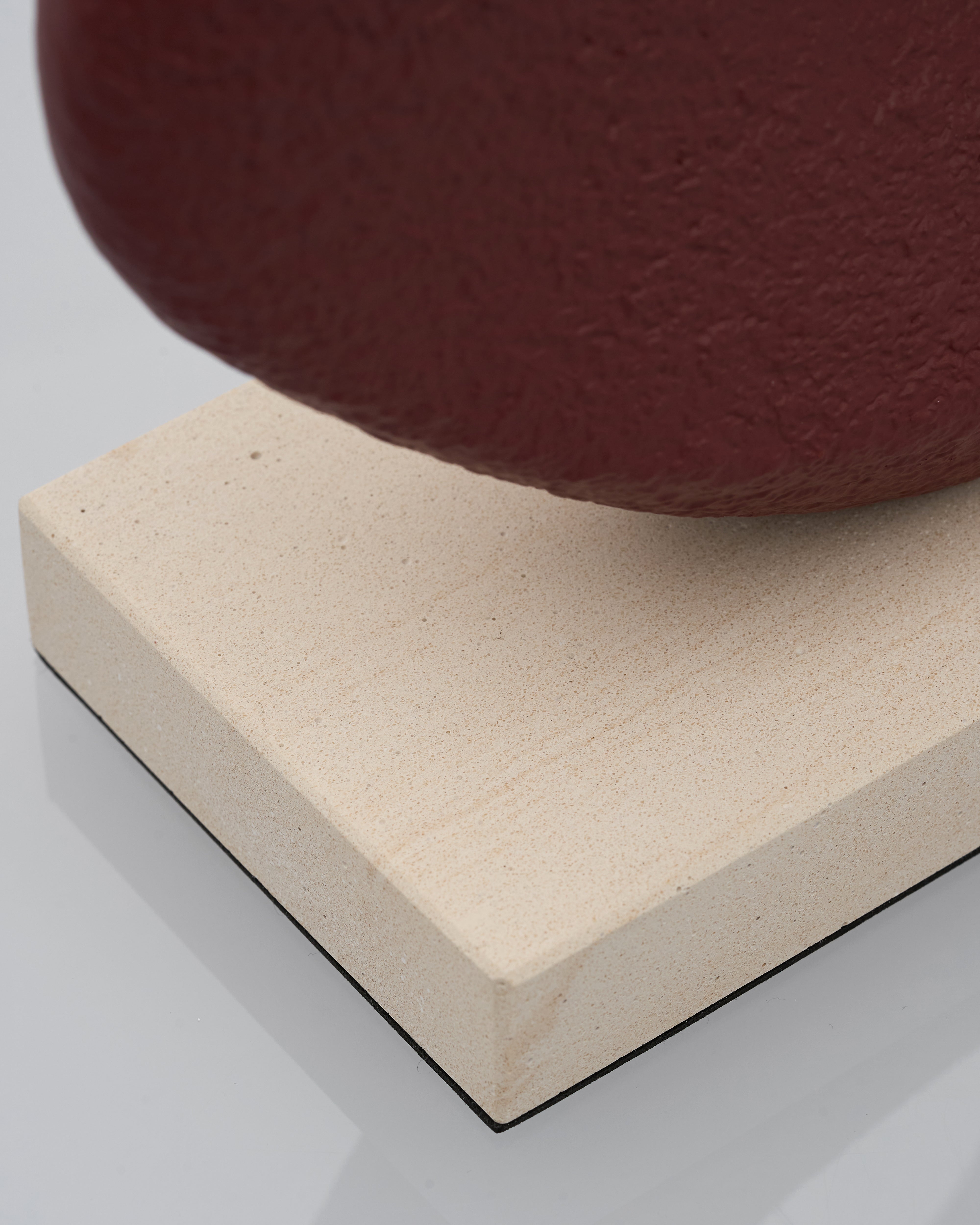 Close-up of a red sculpture ceramic on a beige foam block with a white background