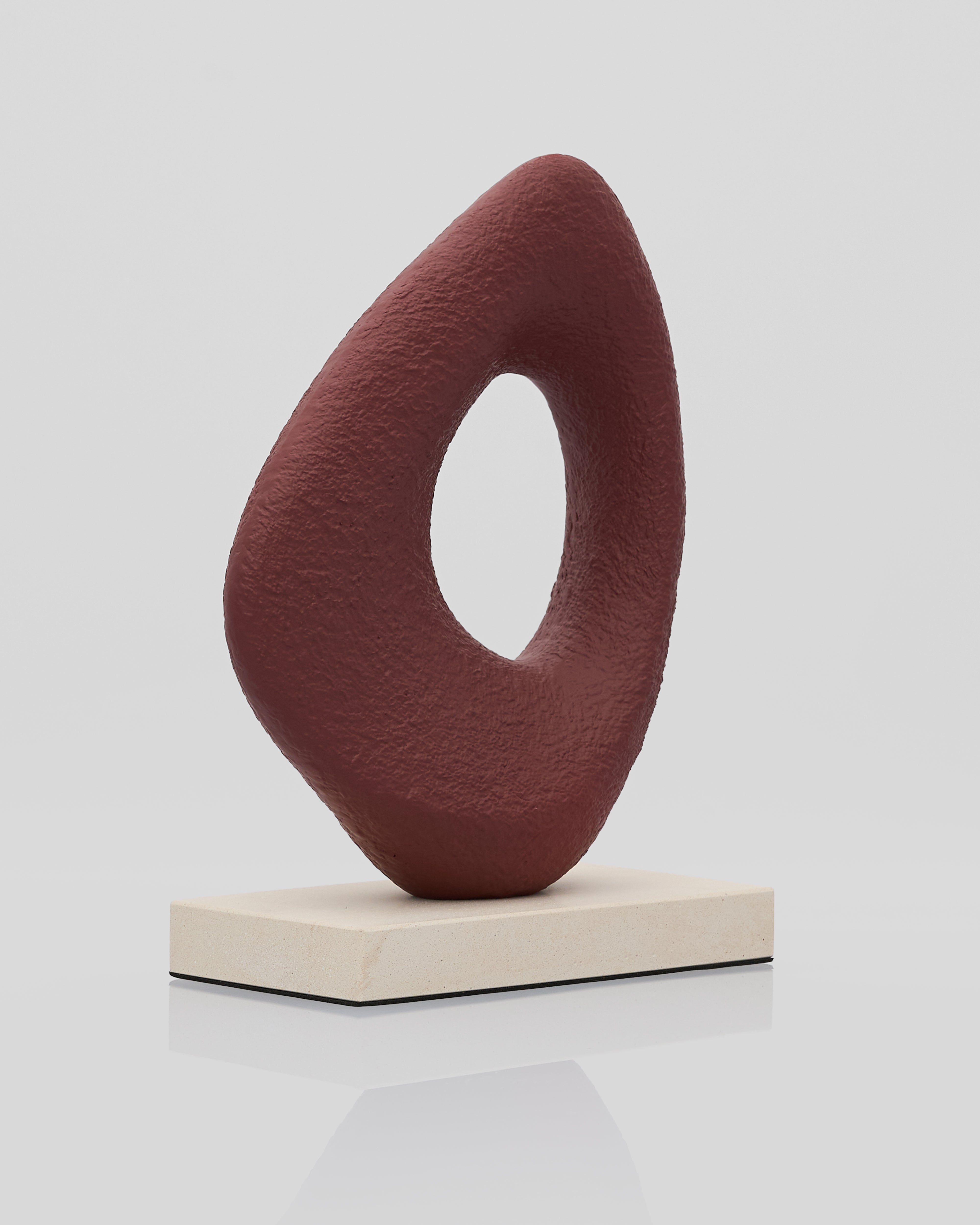 Abstract sculpture on a white platform with a plain background maroon