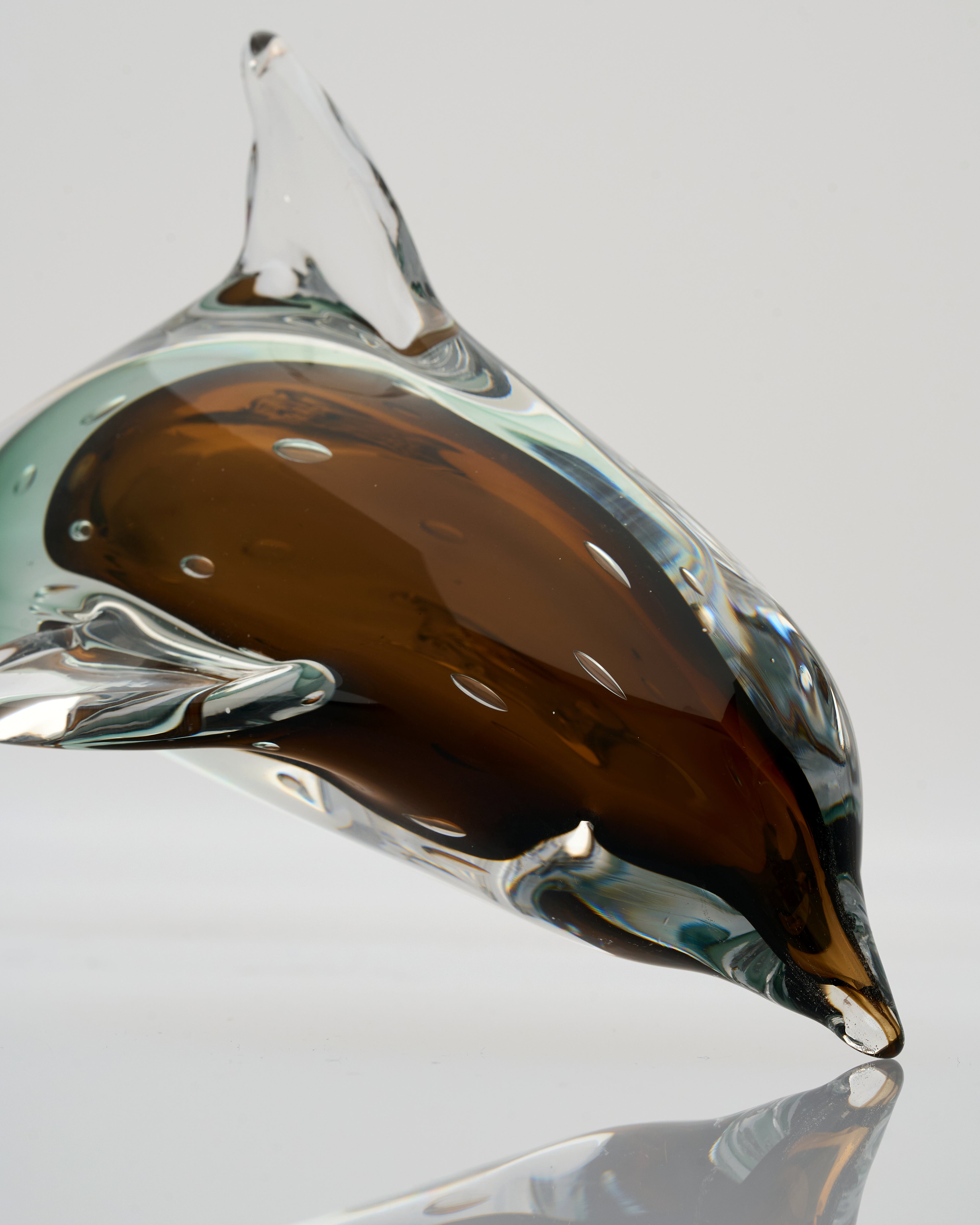 Glass sculpture of a droplet with brown and clear colors on a reflective surface.