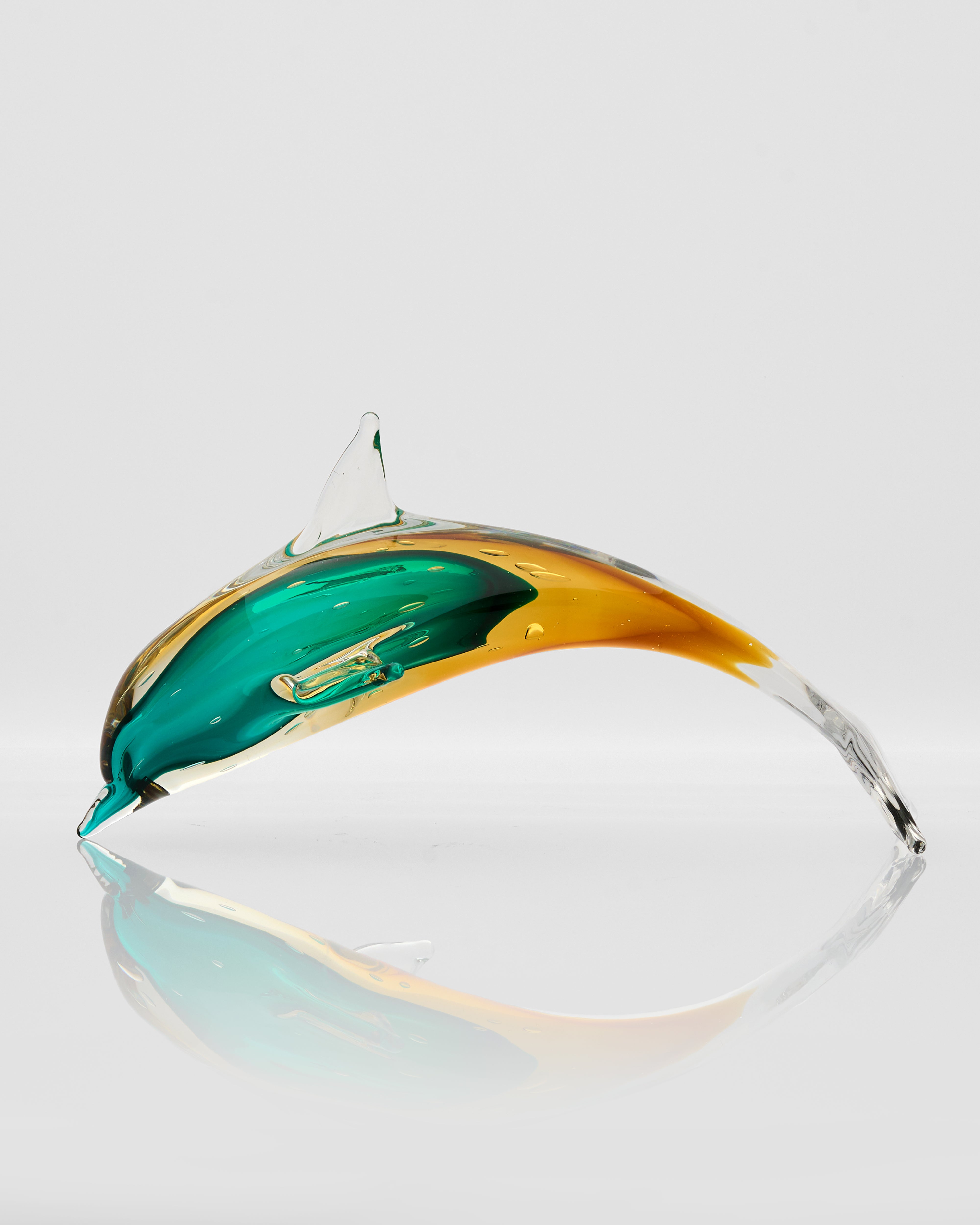 Glass sculpture of a fish with green and gold colors on a light gray background