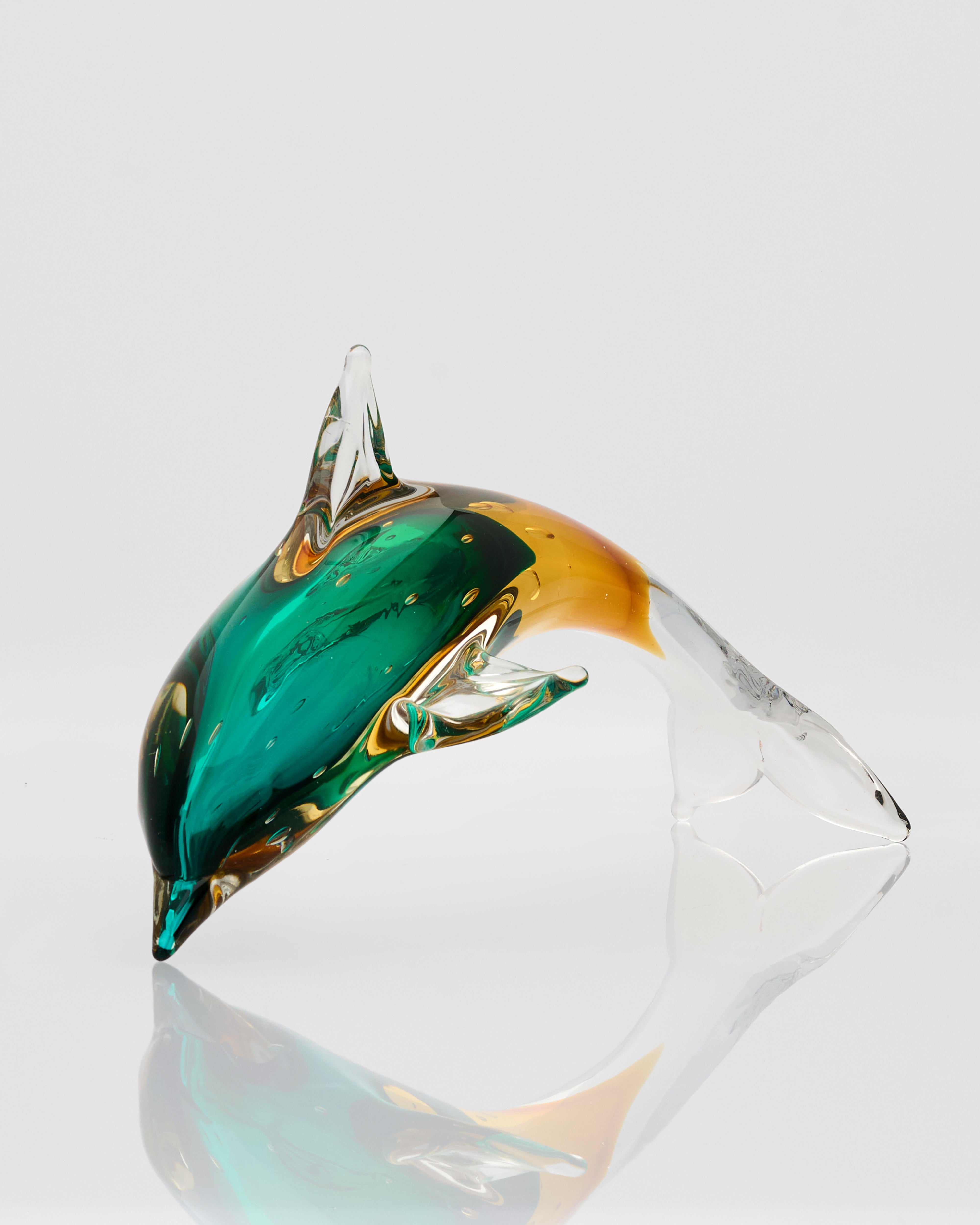 Glass sculpture of a fish with green and gold colors on a white background