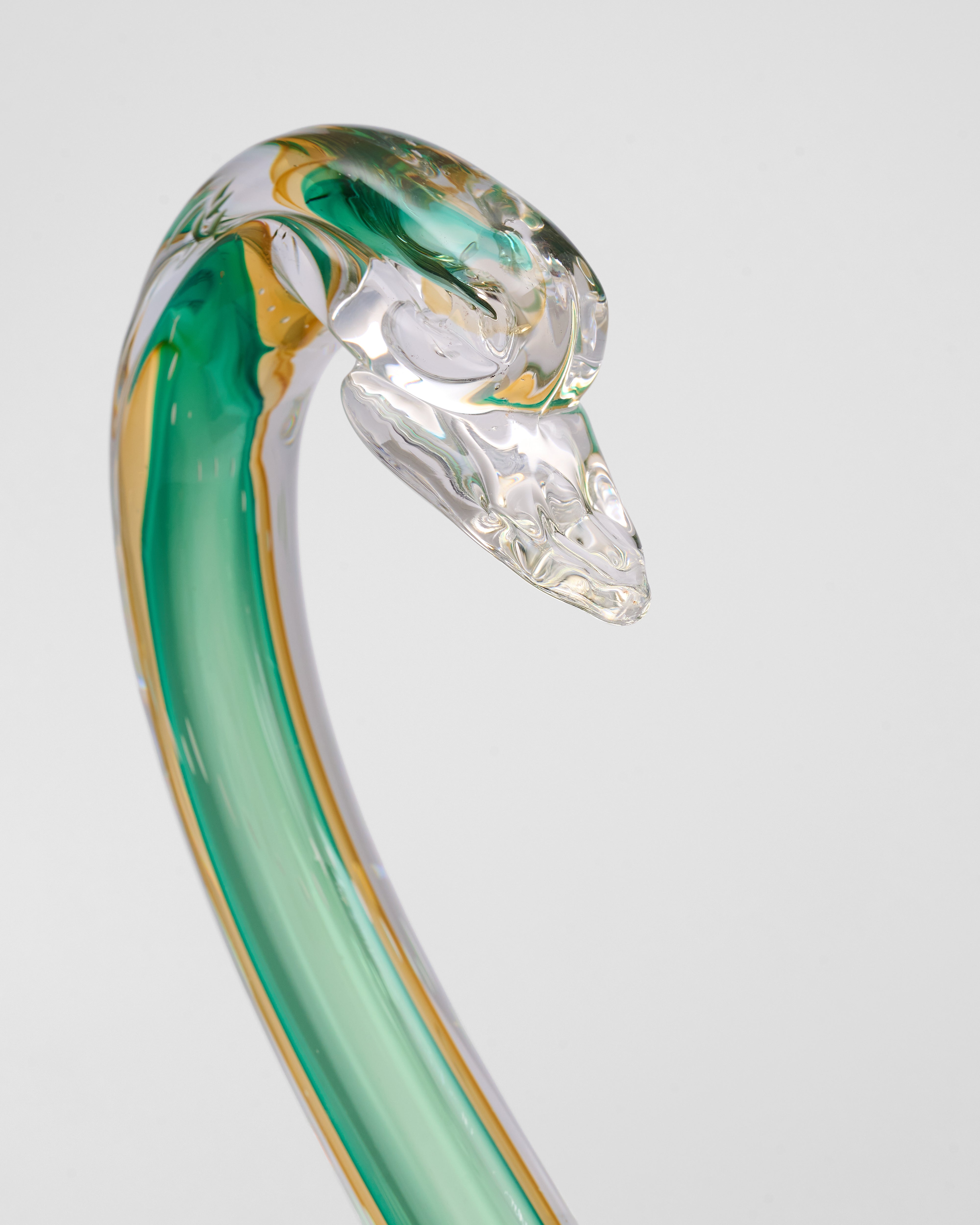 Glass sculpture of a swan with green and clear colors on a light gray background