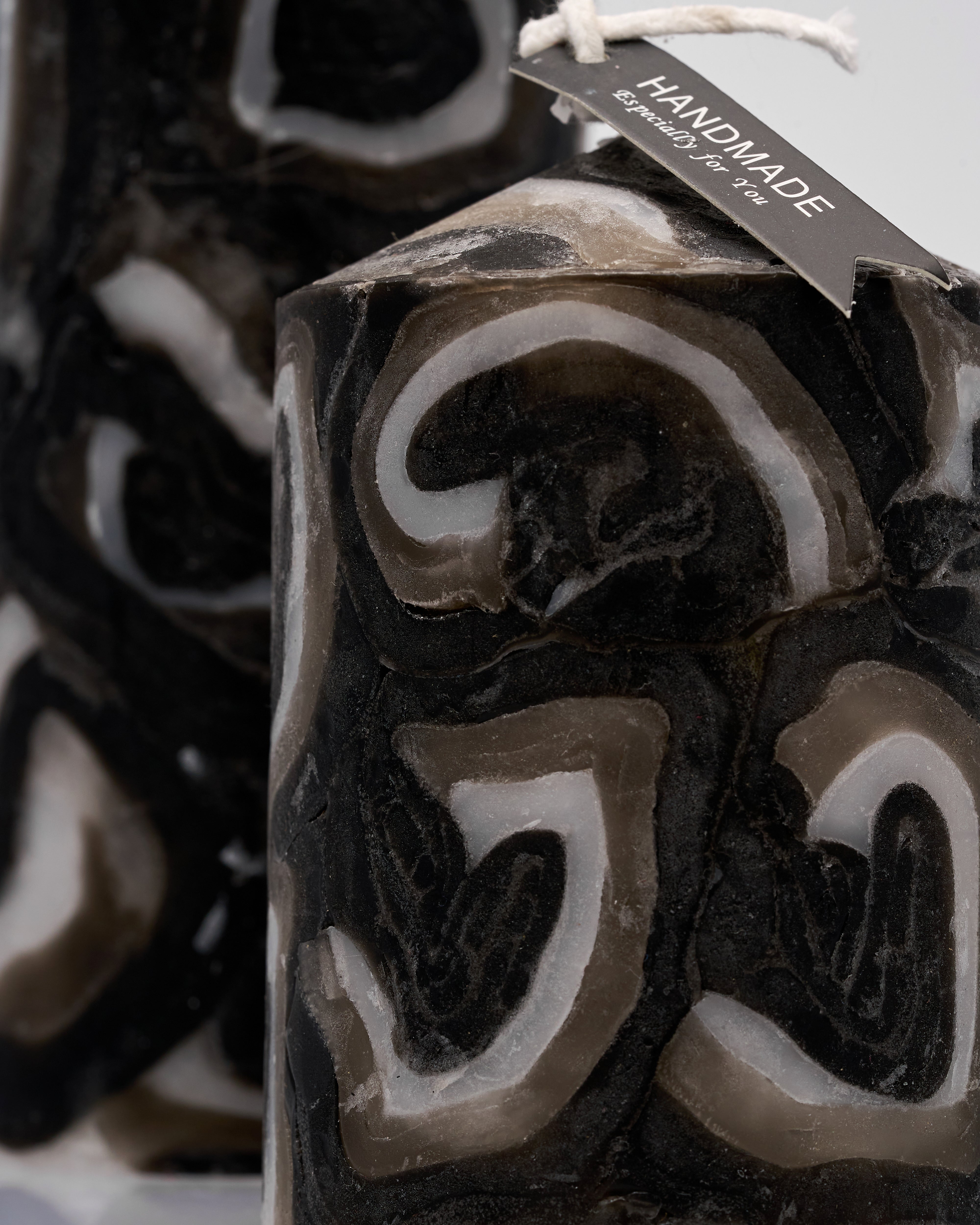 Close-up of a handmade candle with decorative patterns and a visible brand tag.
