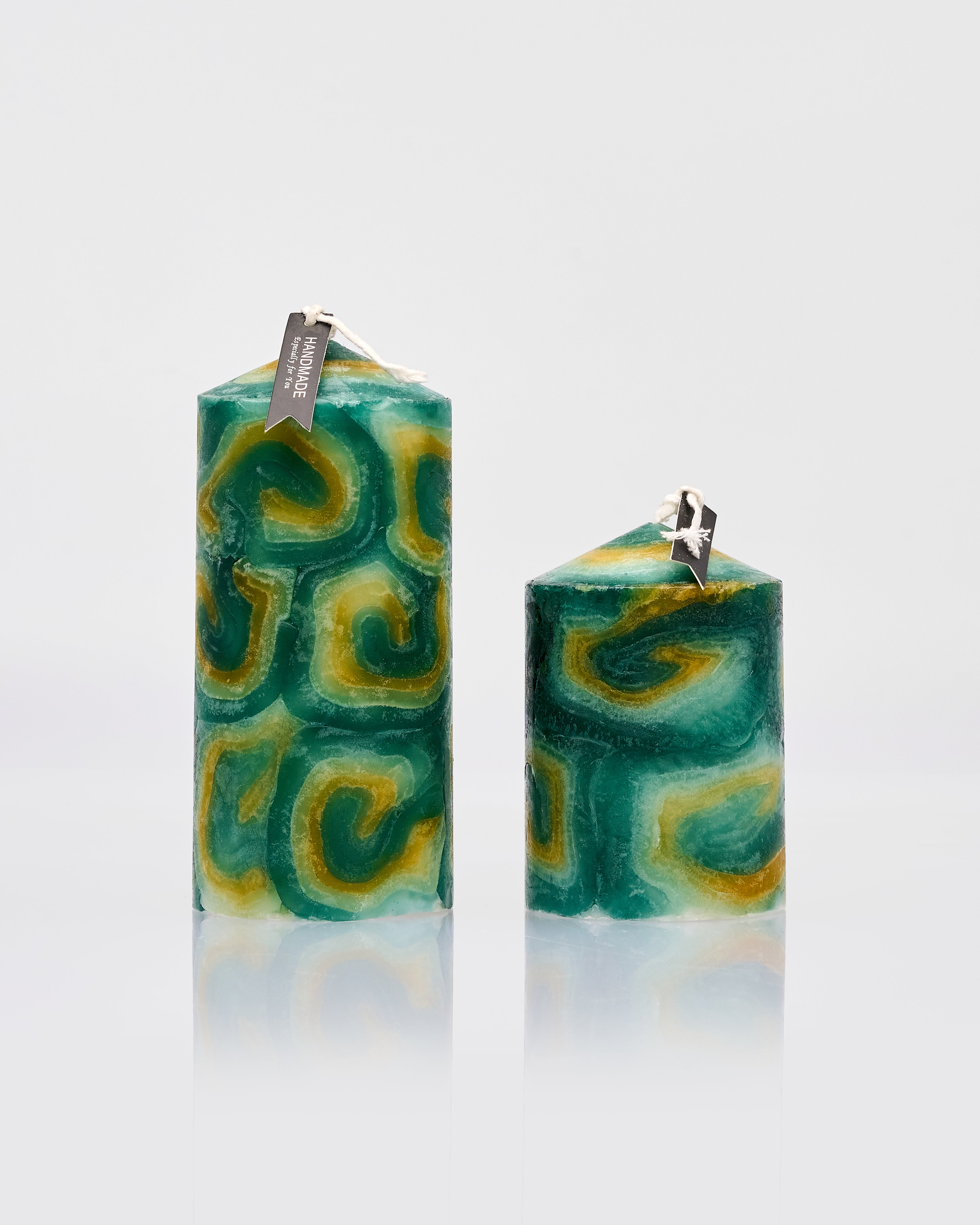Two green and yellow patterned candles on a light gray background