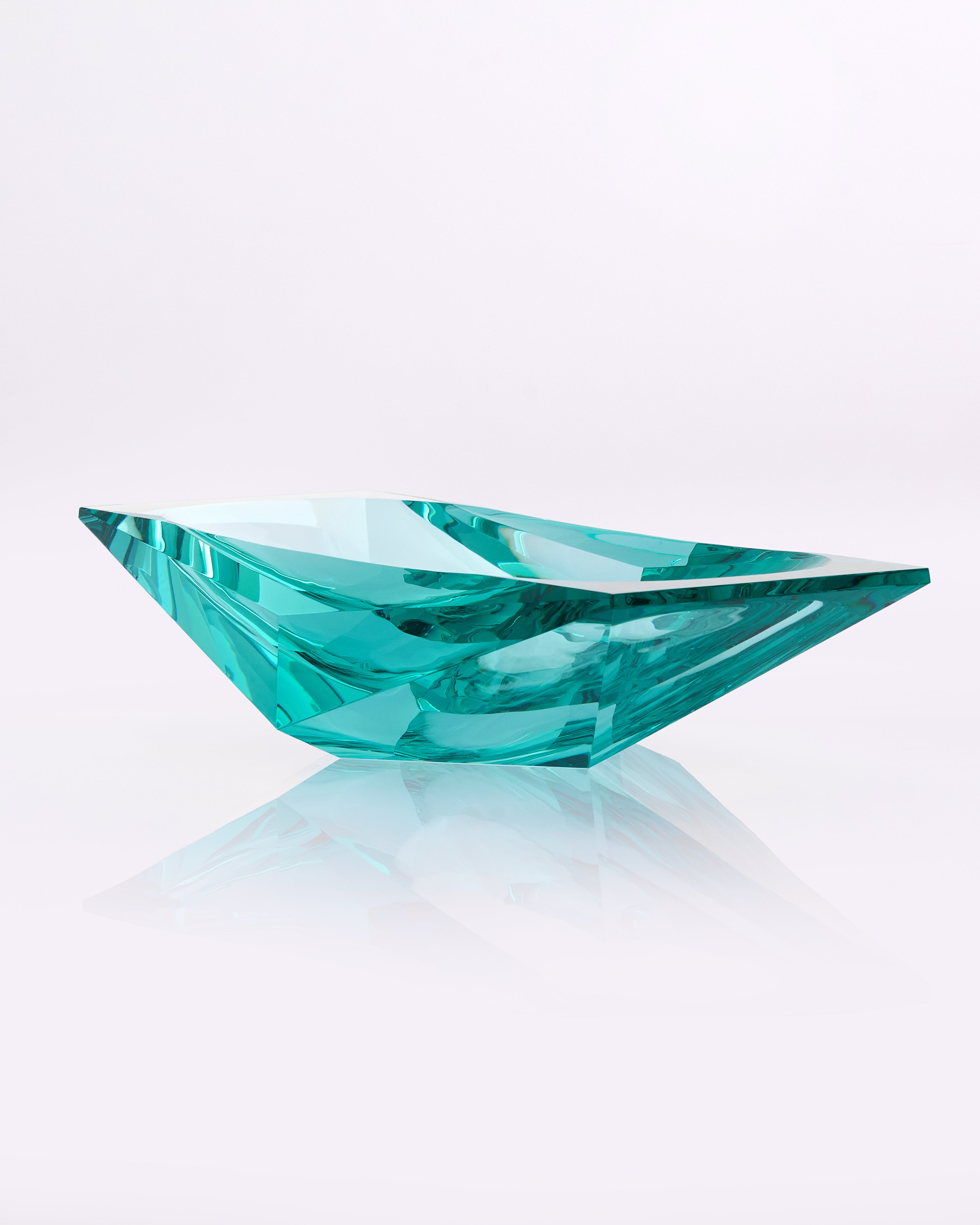 Teal gemstone on a reflective surface with a light gray background