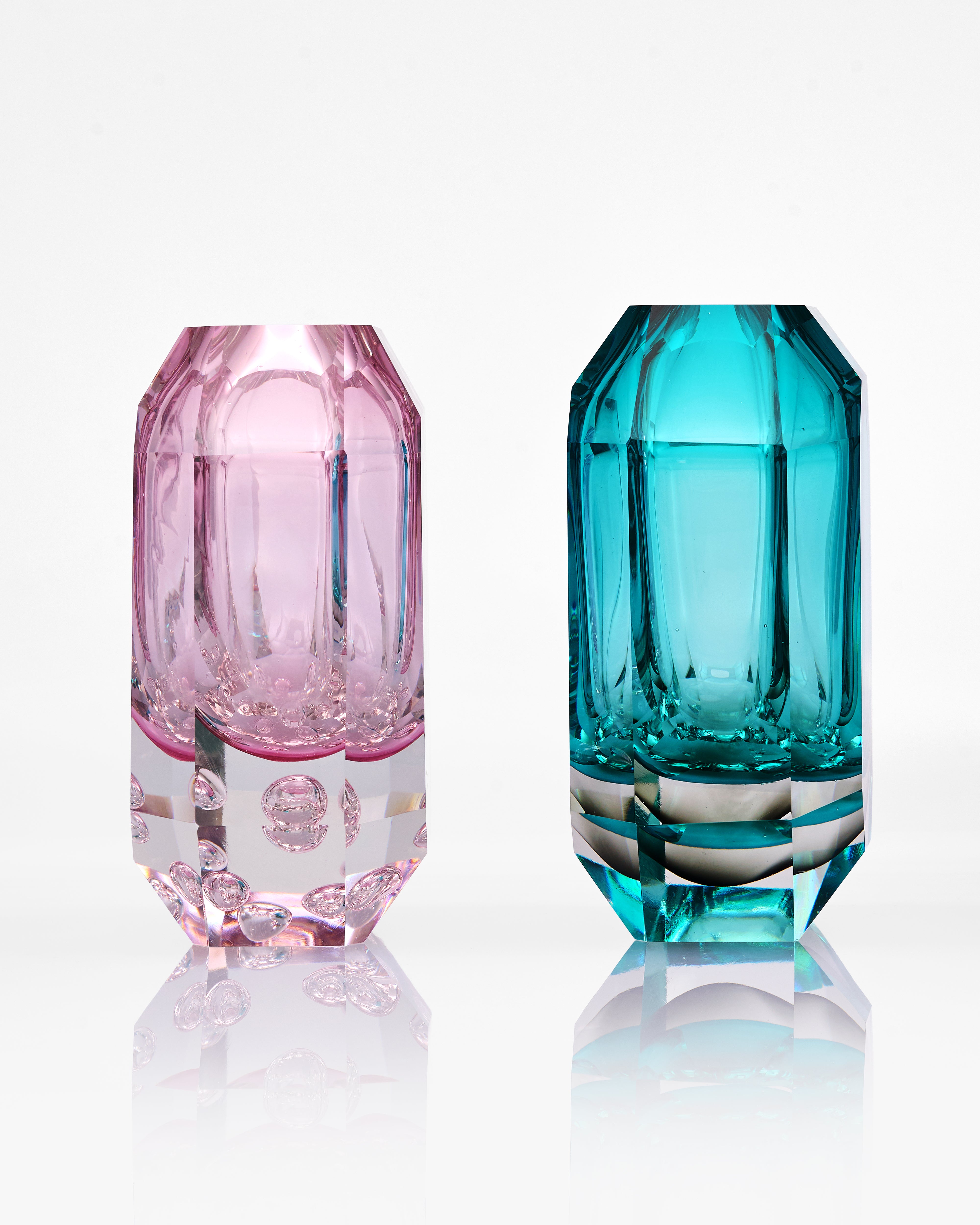 Two faceted glass vases, one pink and one blue, on a white background