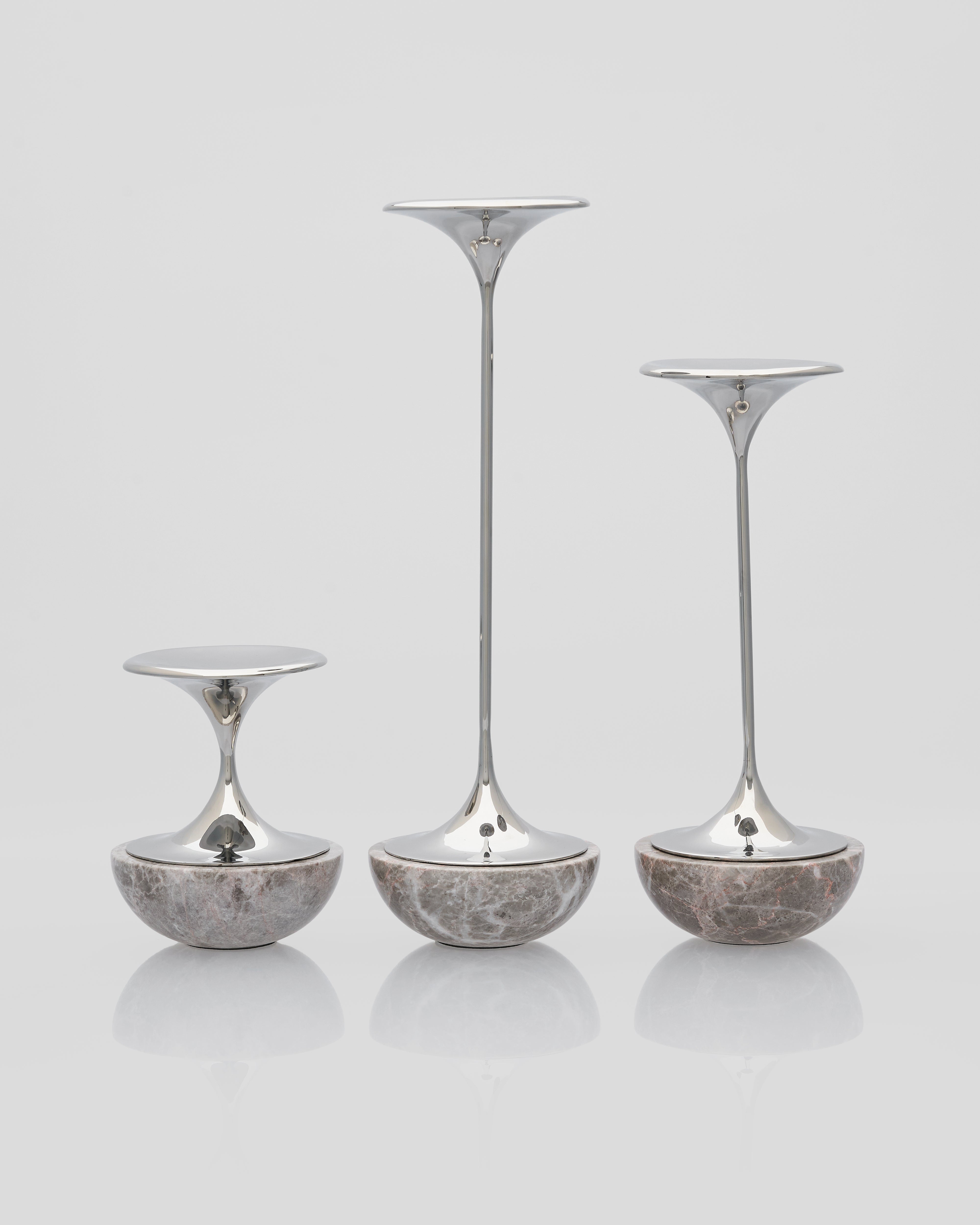 Set of three silver candle holders with textured bases on a light gray background