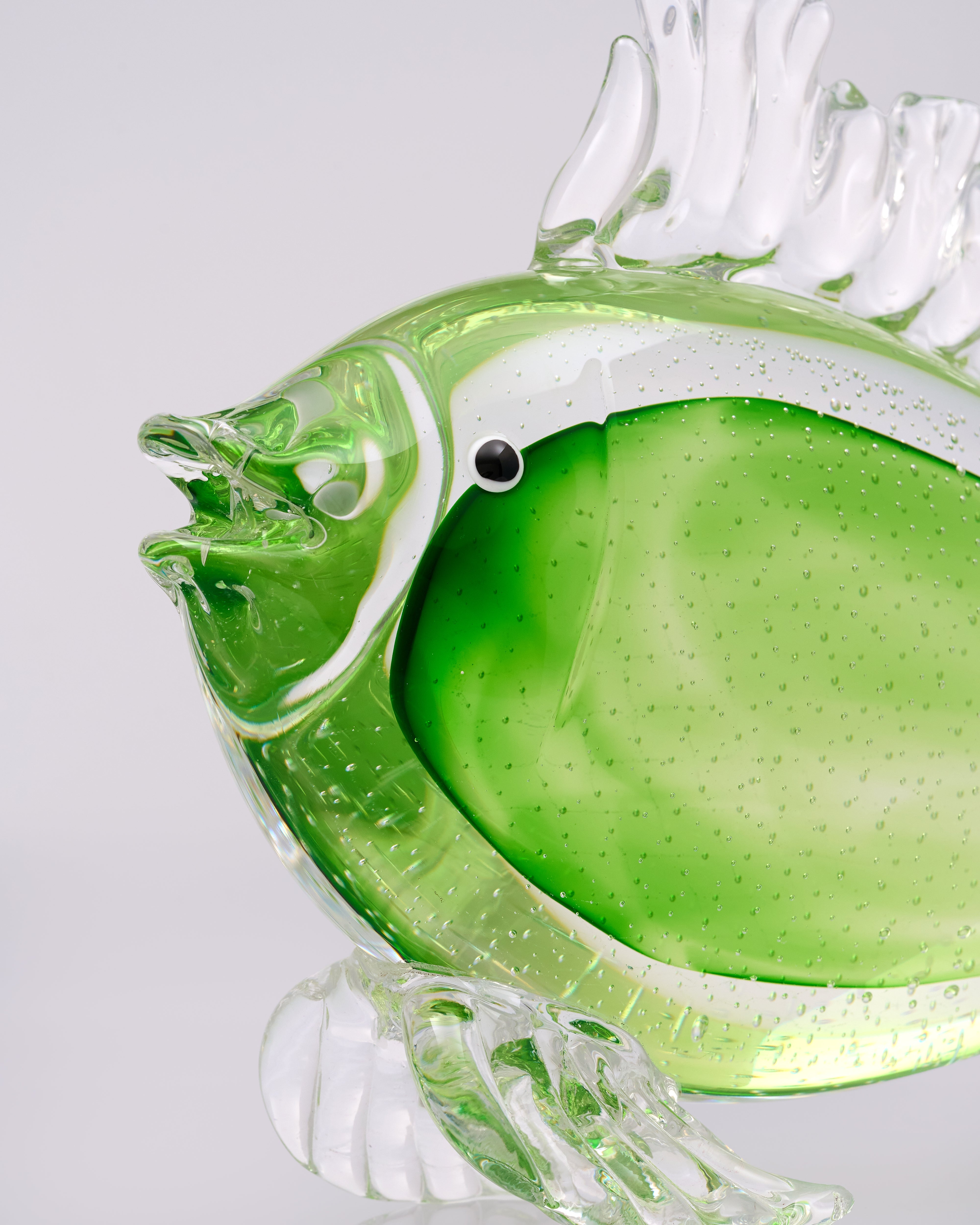 Glass fish-shaped object with a green body and clear wings on a light gray background