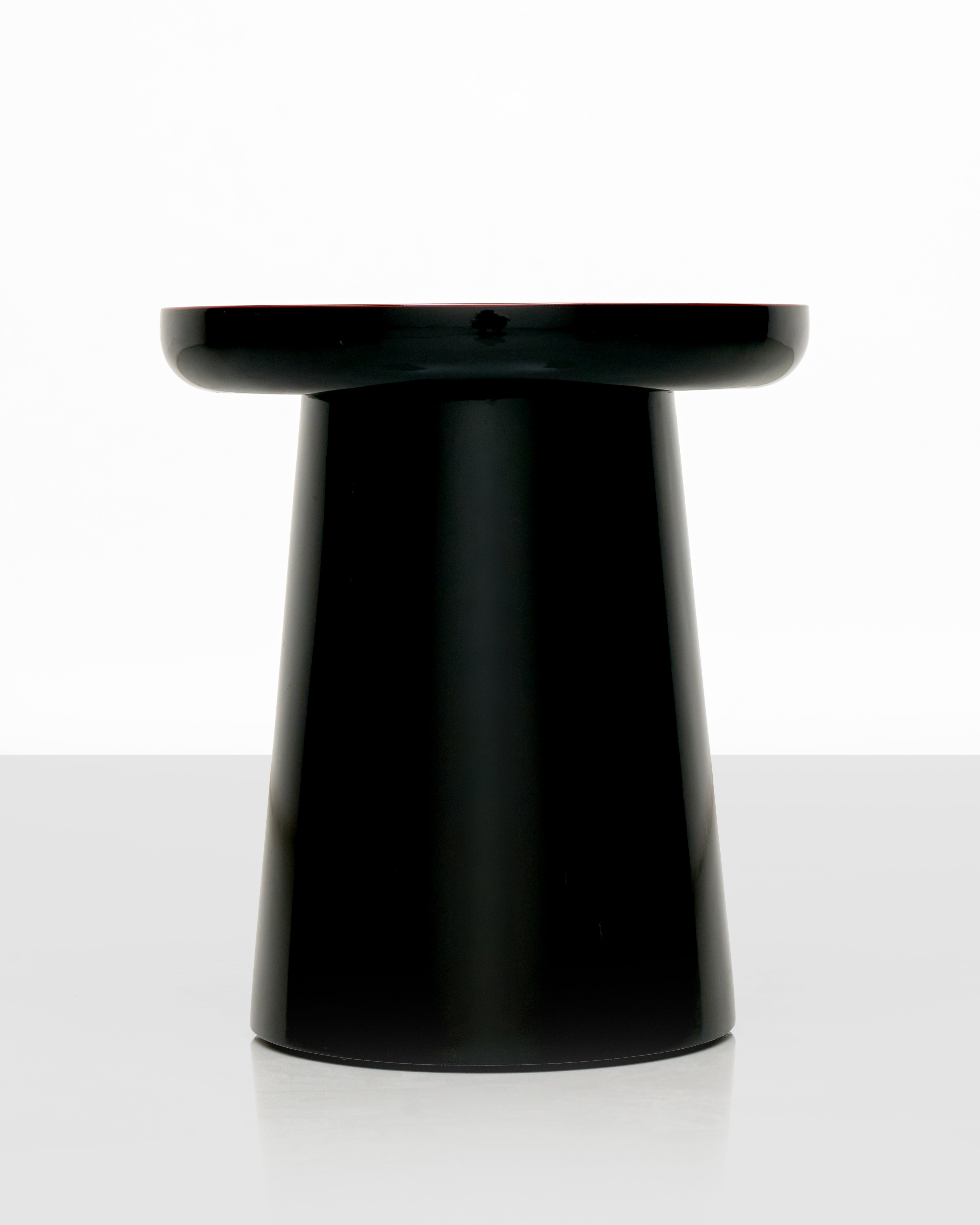 Black cylindrical side table with red top on a white background