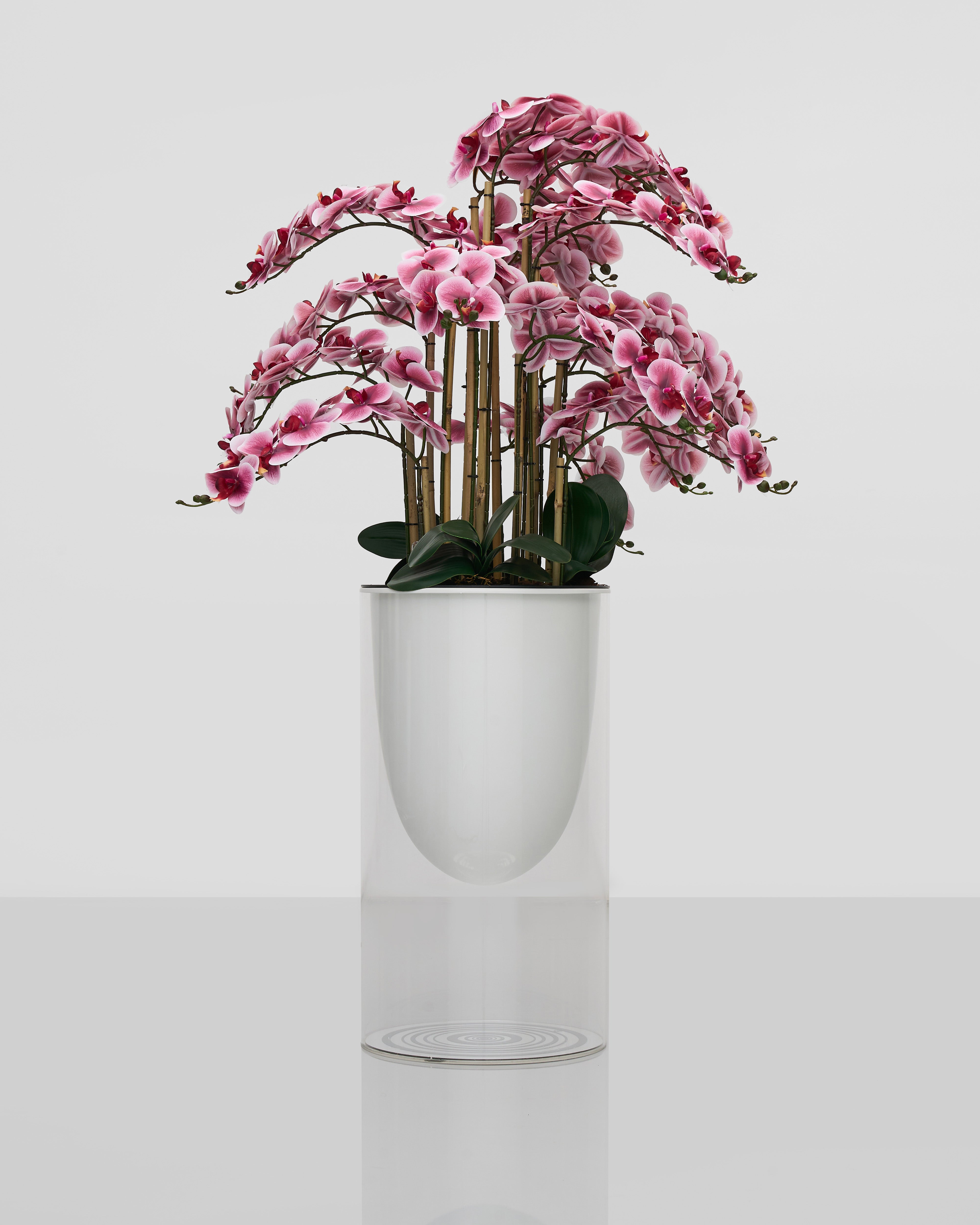 Pink artificial flower arrangement in a white pot on a light gray background