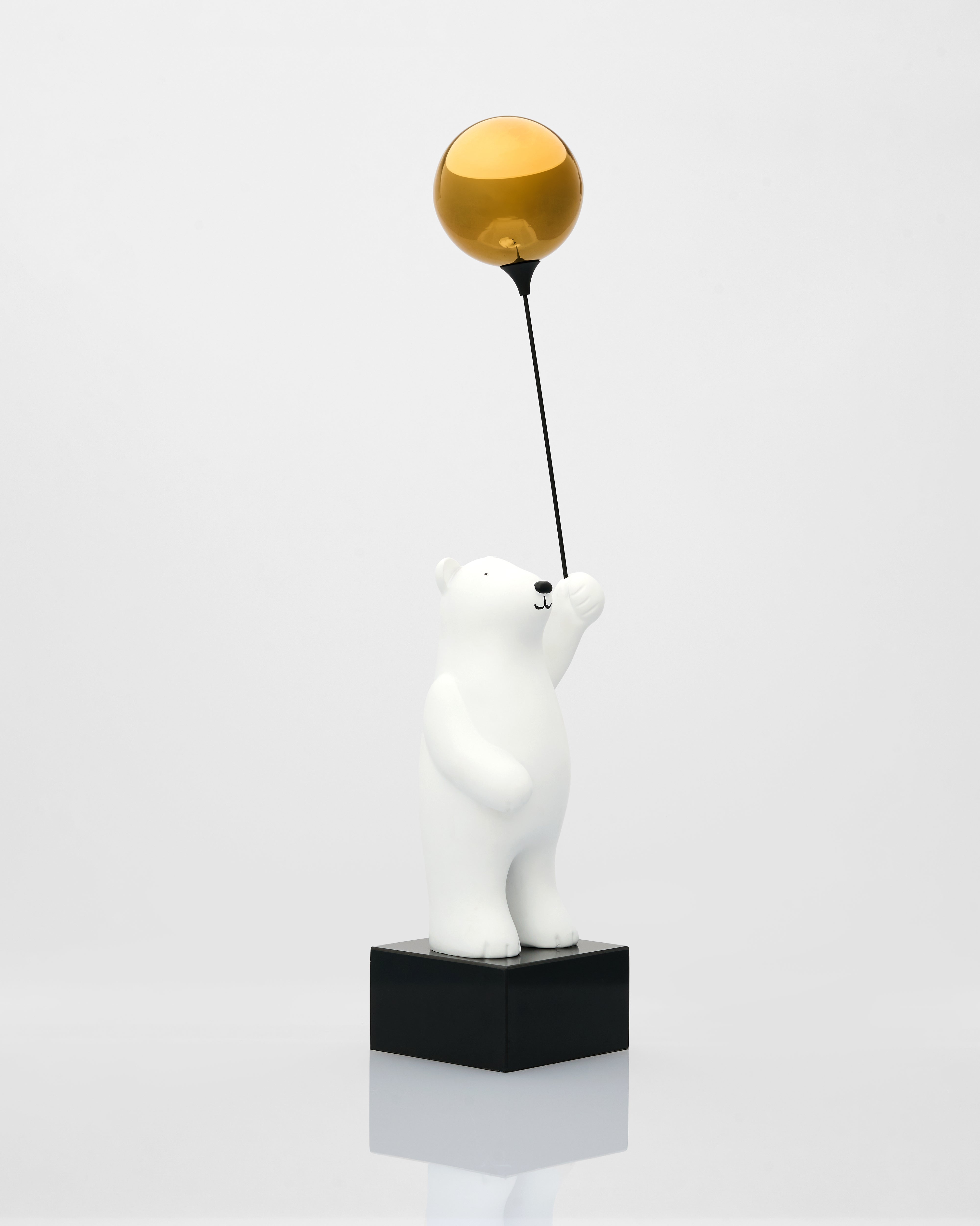 White polar bear figurine holding a gold ball on a white background