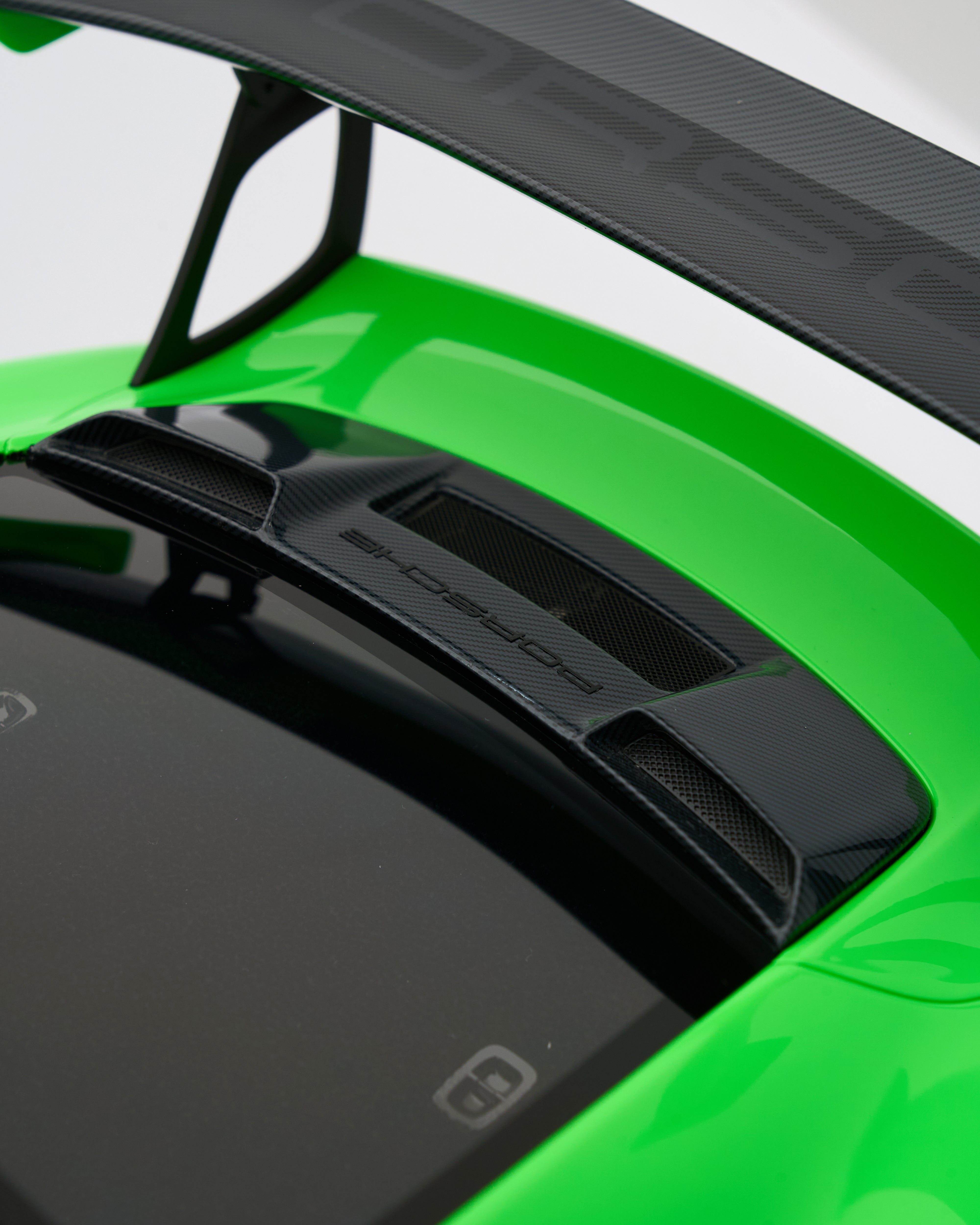 Close-up of a car spoiler with 'Porsche' branding on a green car.