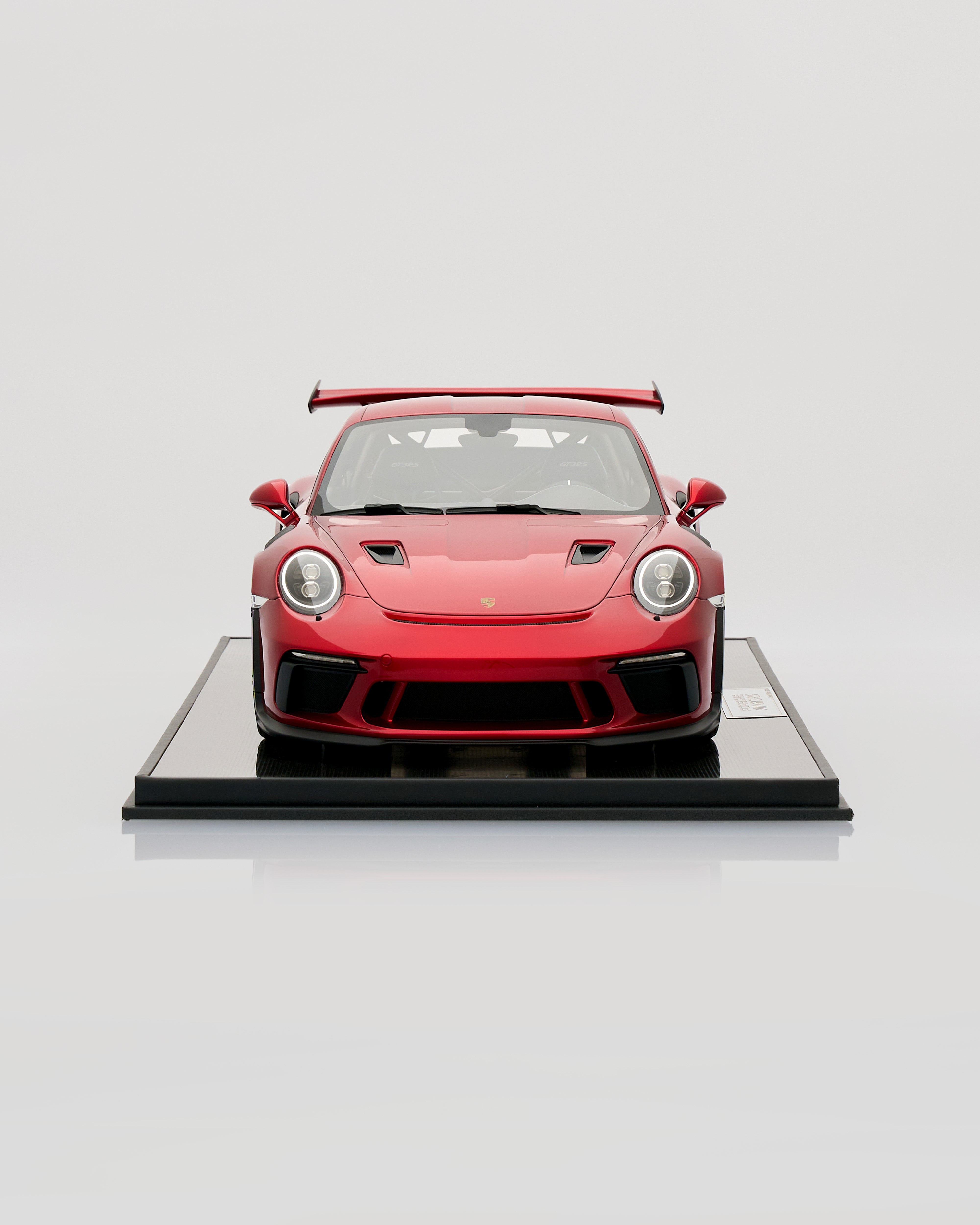 Red sports car model on a reflective black platform with a white background