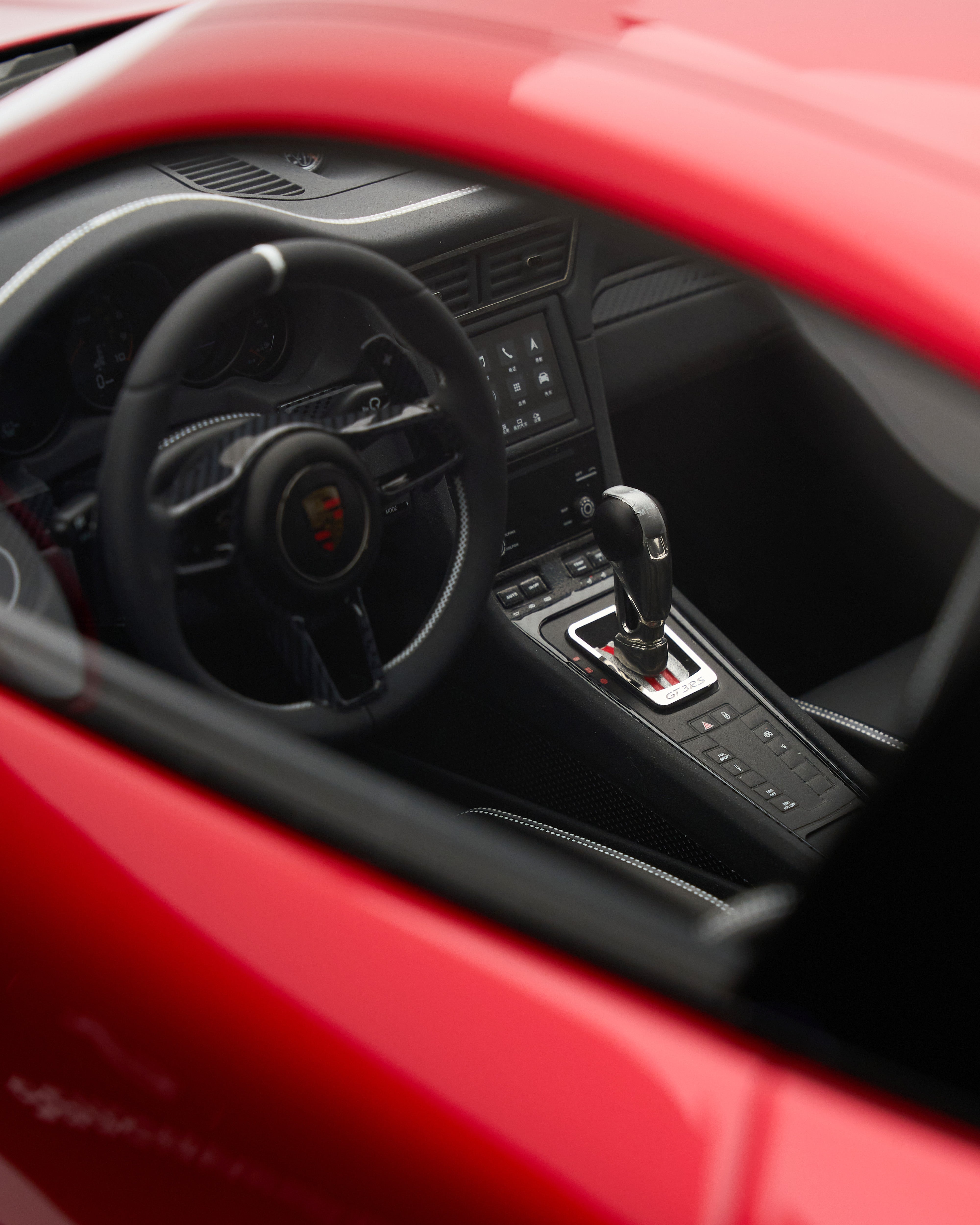 Close-up of a red car's interior with steering wheel and gear shift.
