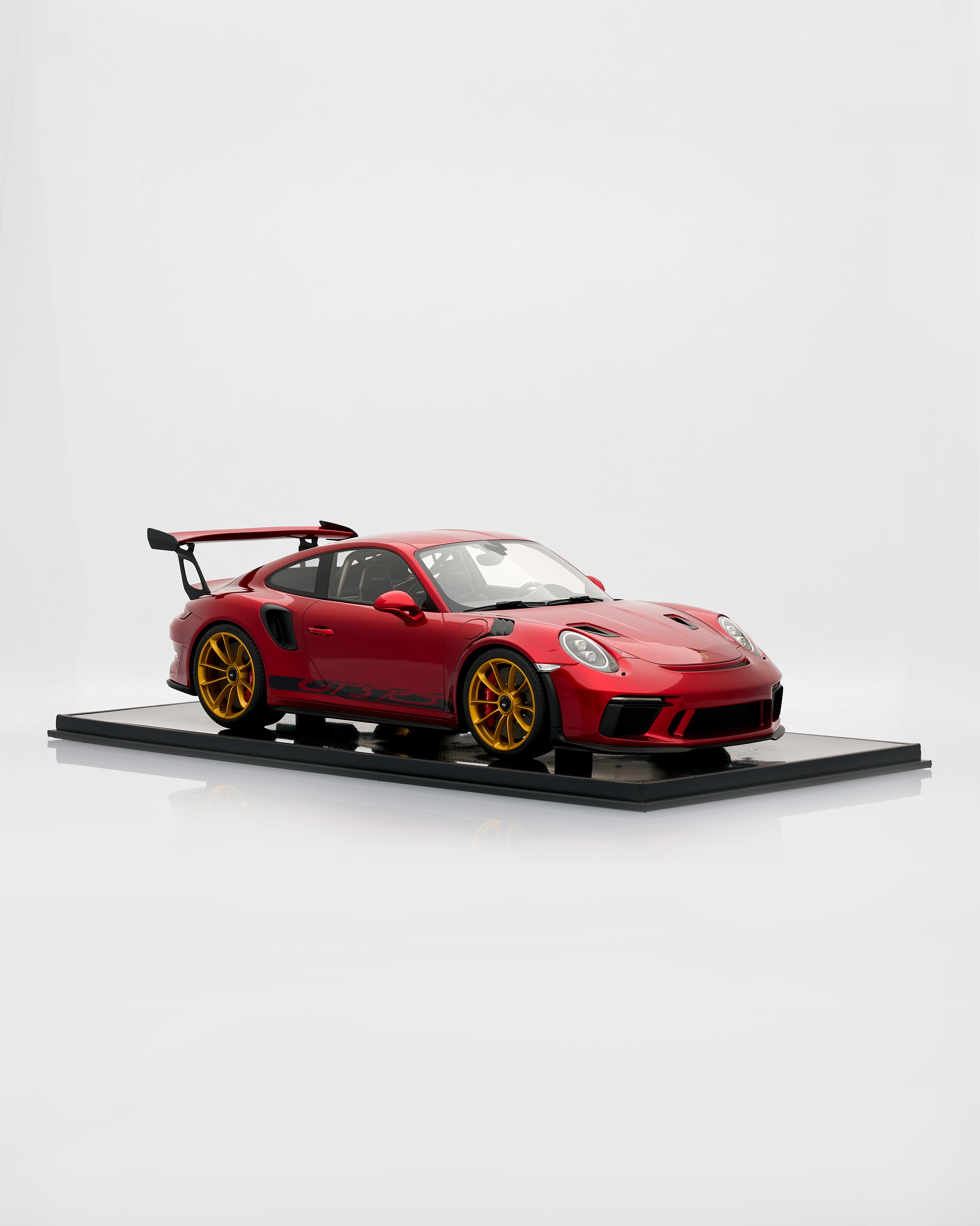 Red sports car model on a black platform with a white background