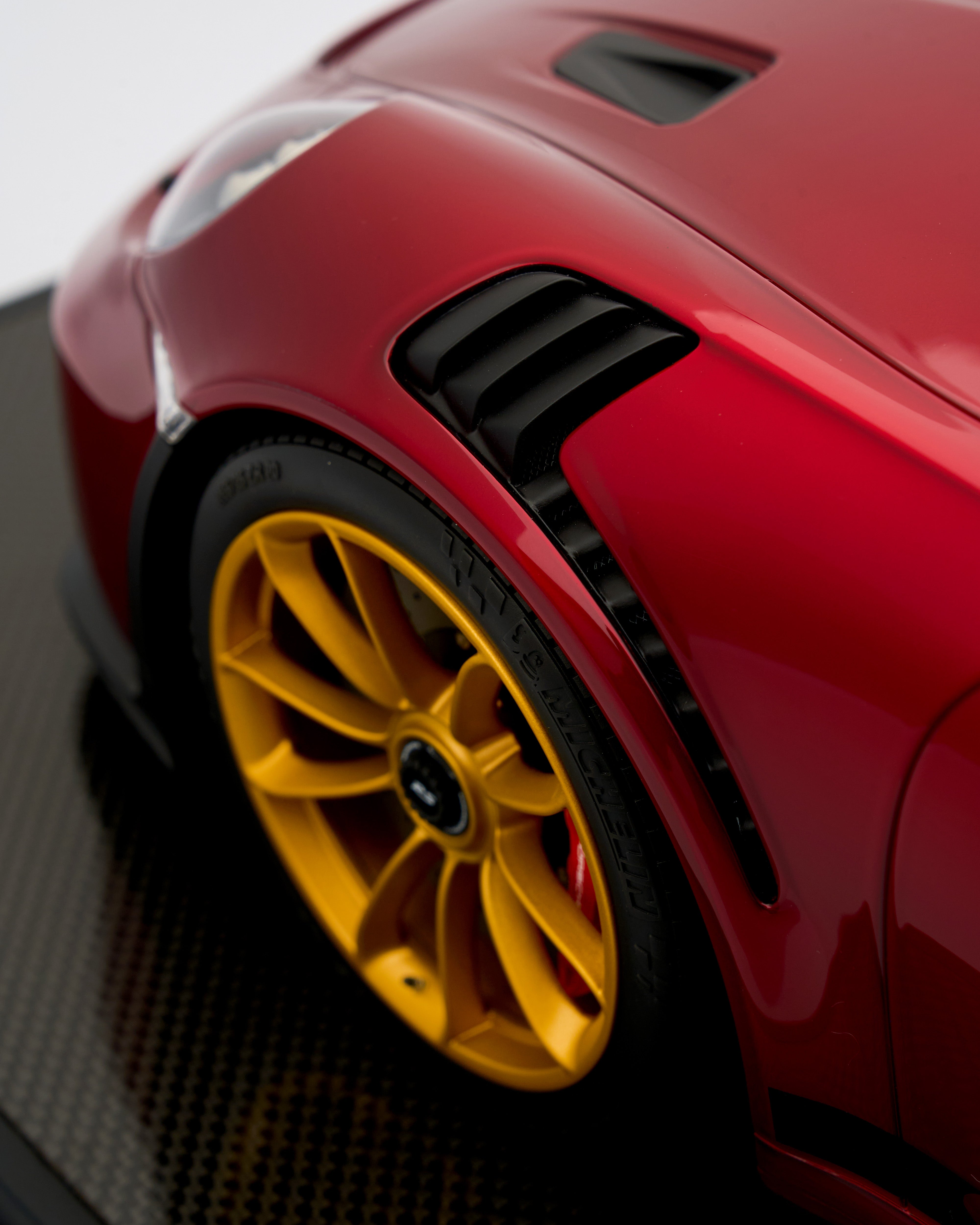 Close-up of a red car with a yellow wheel on a dark textured surface
