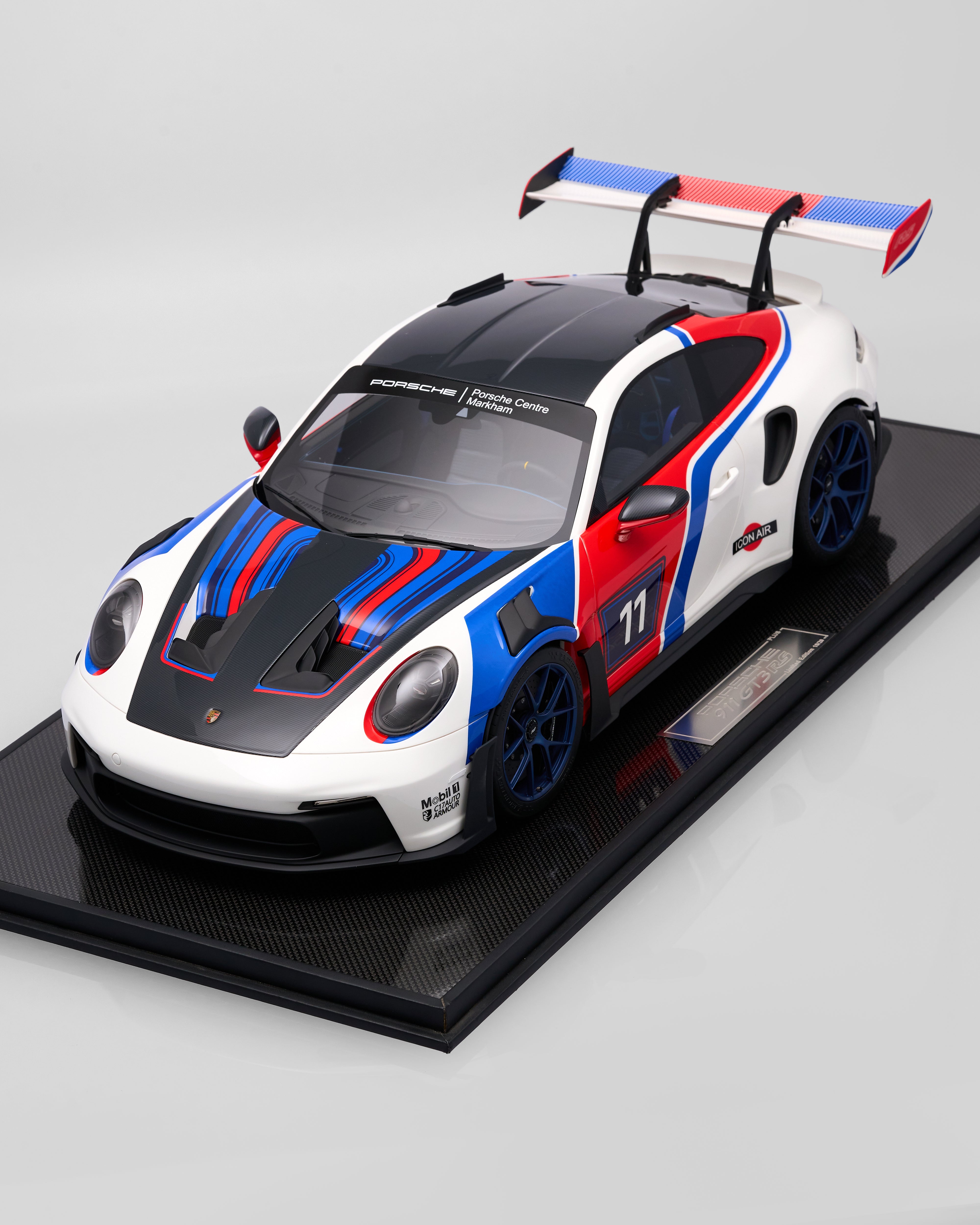 Model of a Porsche sports car with red, white, and blue design on a black platform.