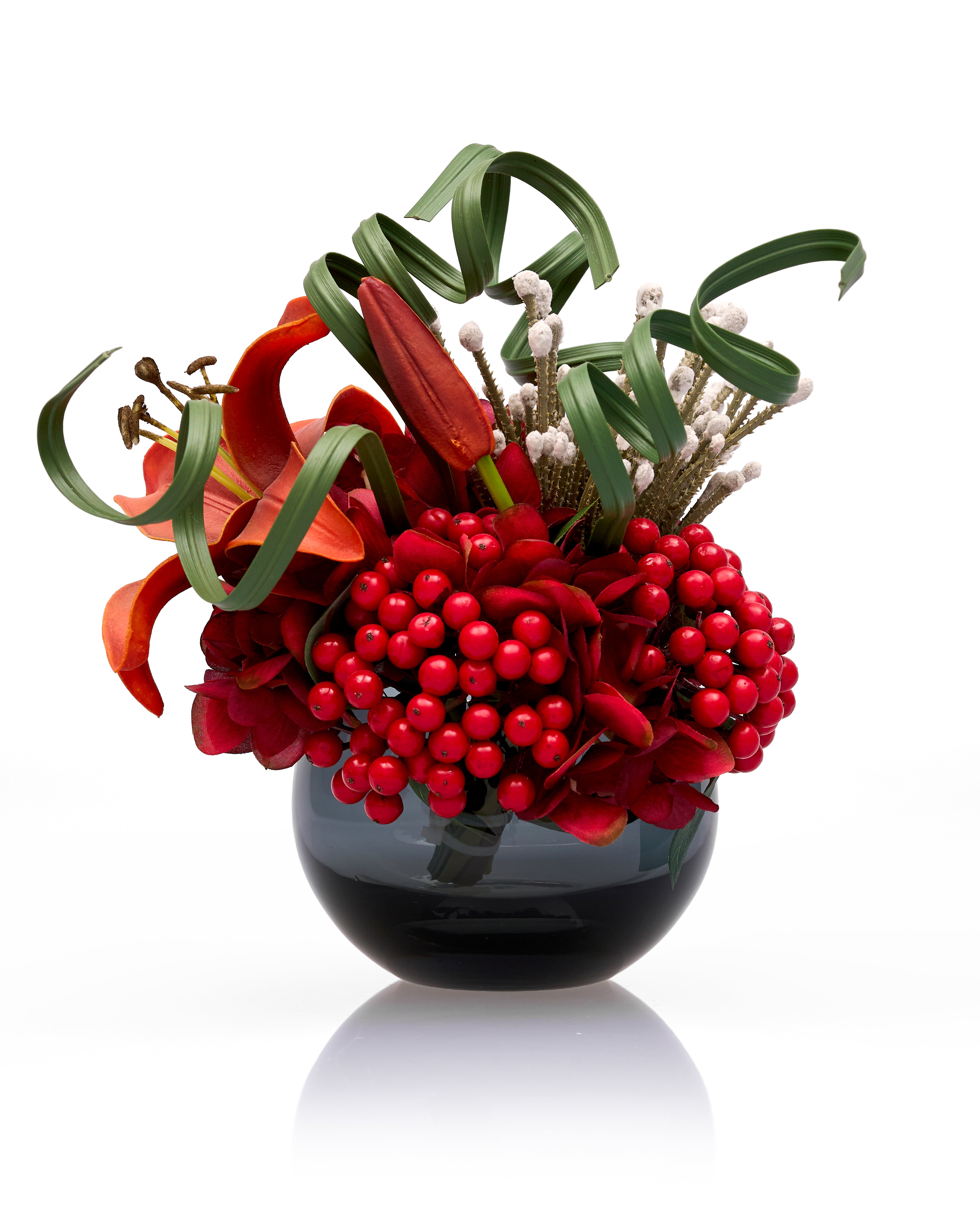 Decorative flower arrangement with red berries and green leaves in a black vase on a white background