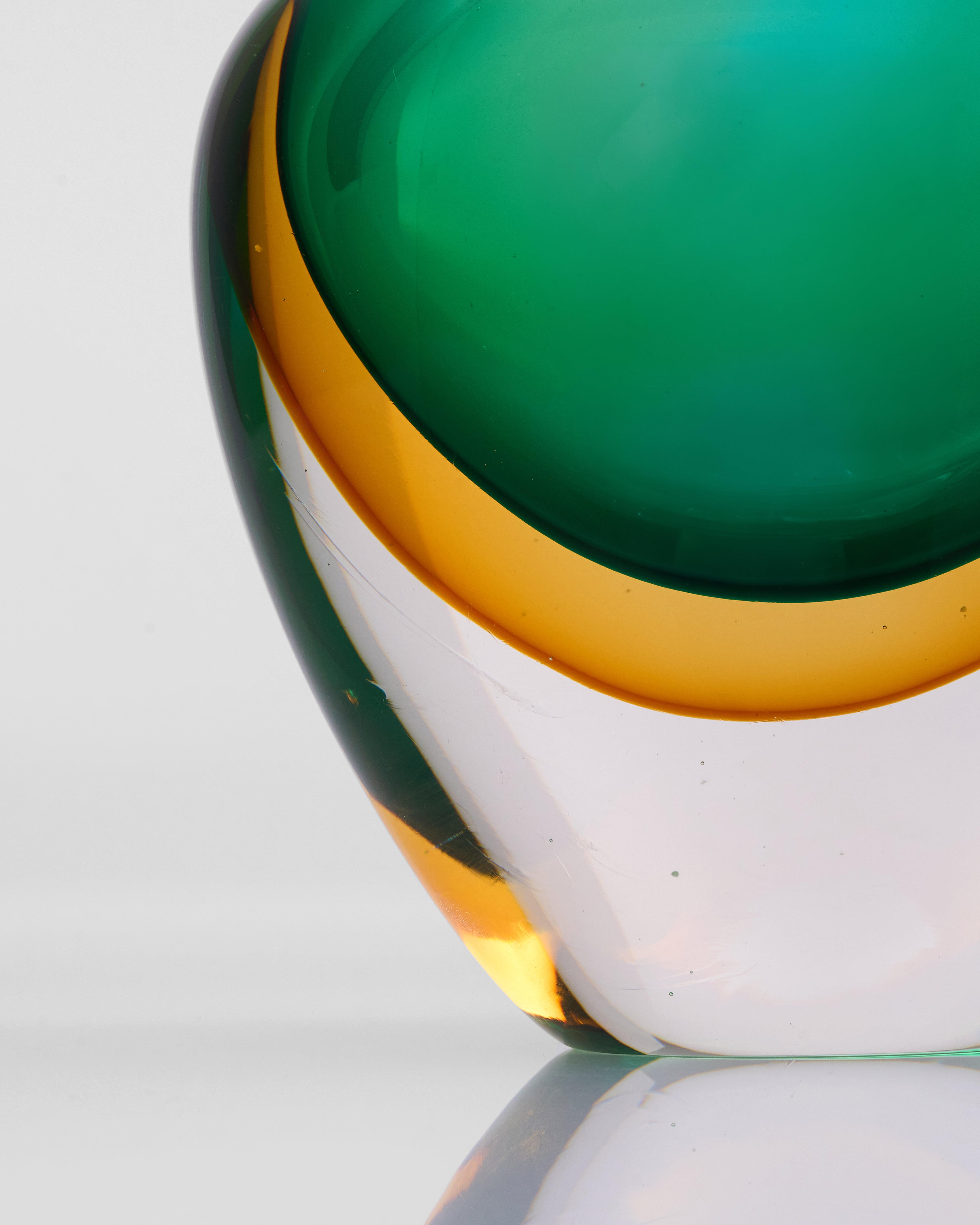 Close-up of a glass object with green, gold, and white colors on a light gray background