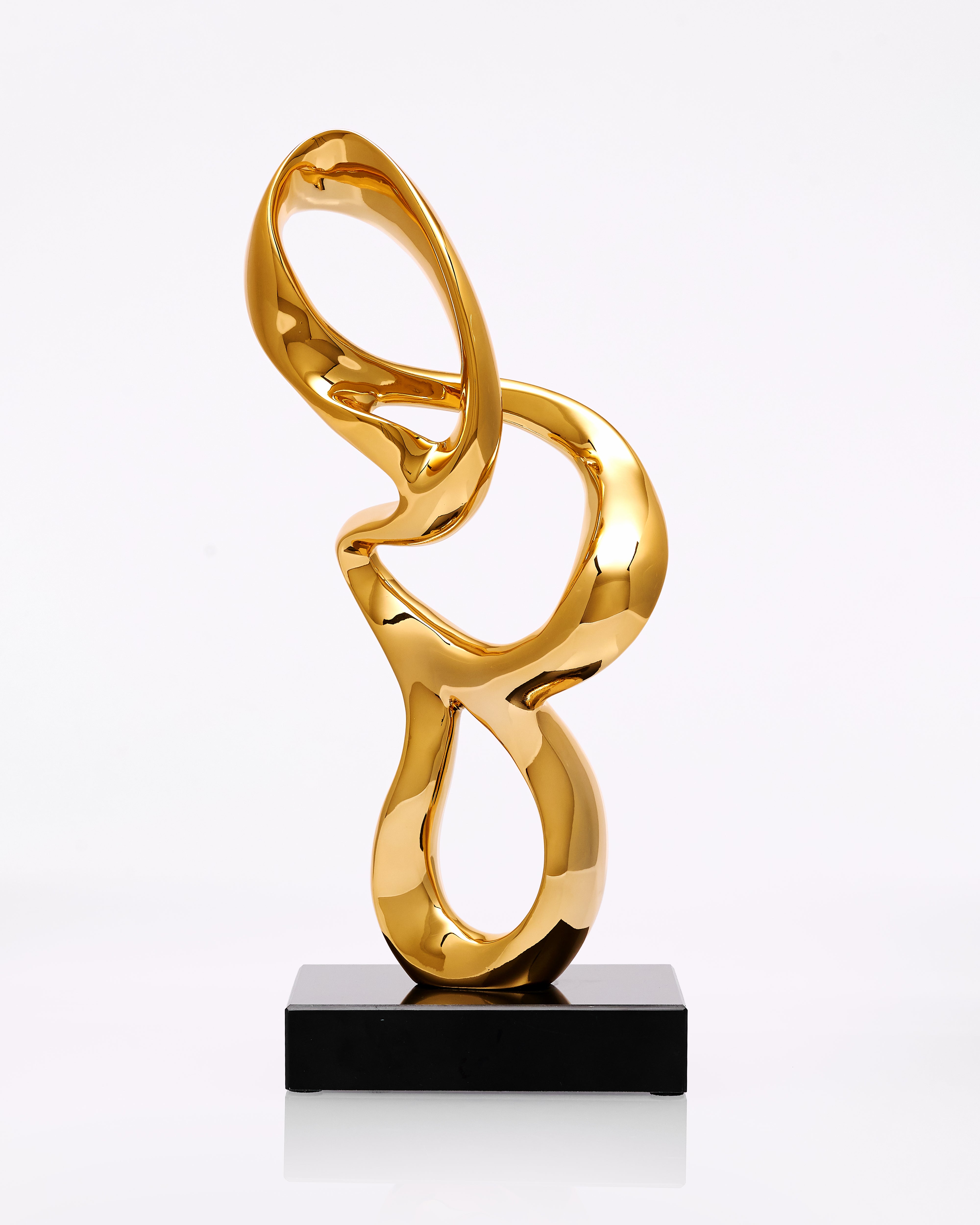 Gold abstract sculpture on a black base against a white background