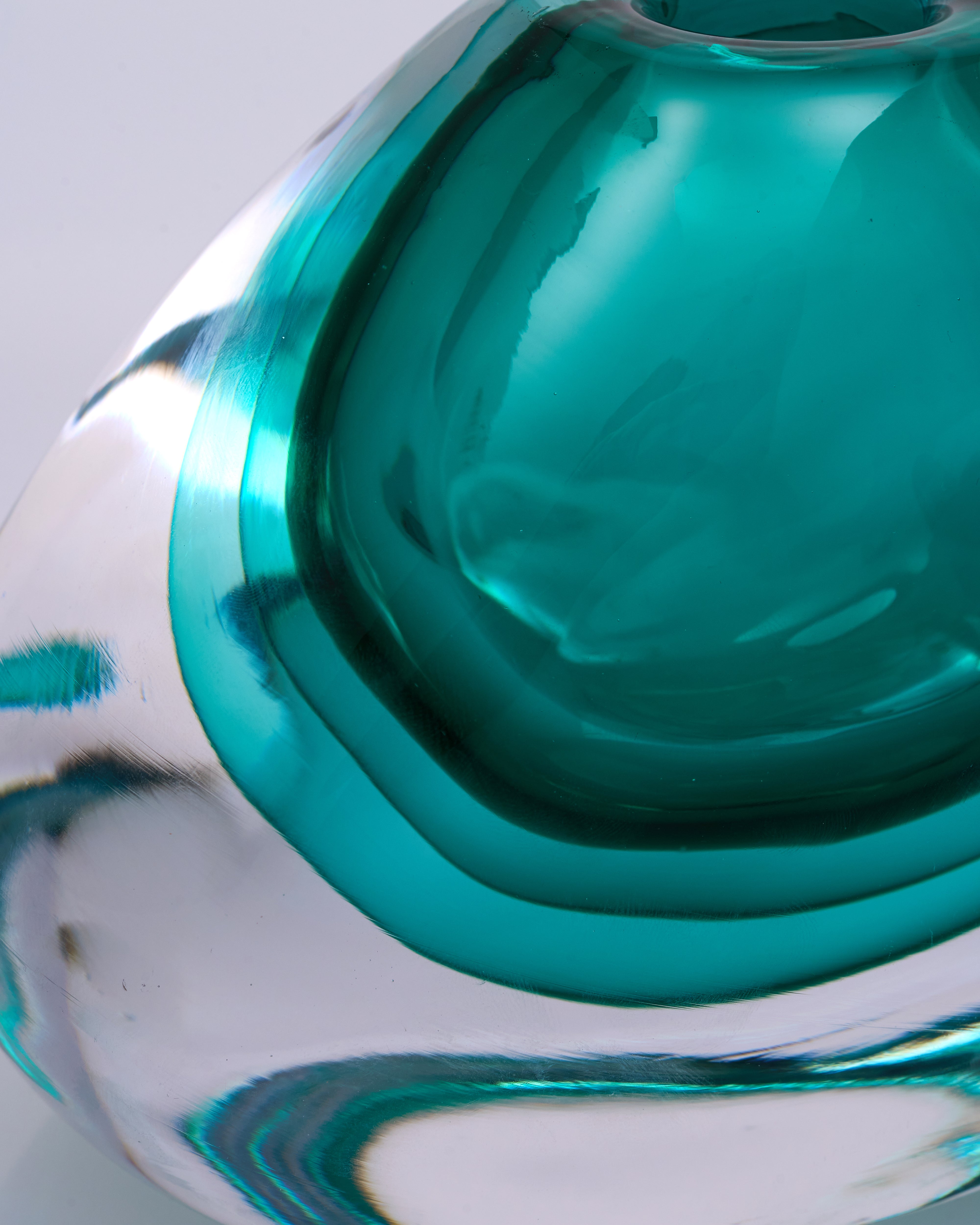 Close-up of a teal glass object with swirling patterns on a white background