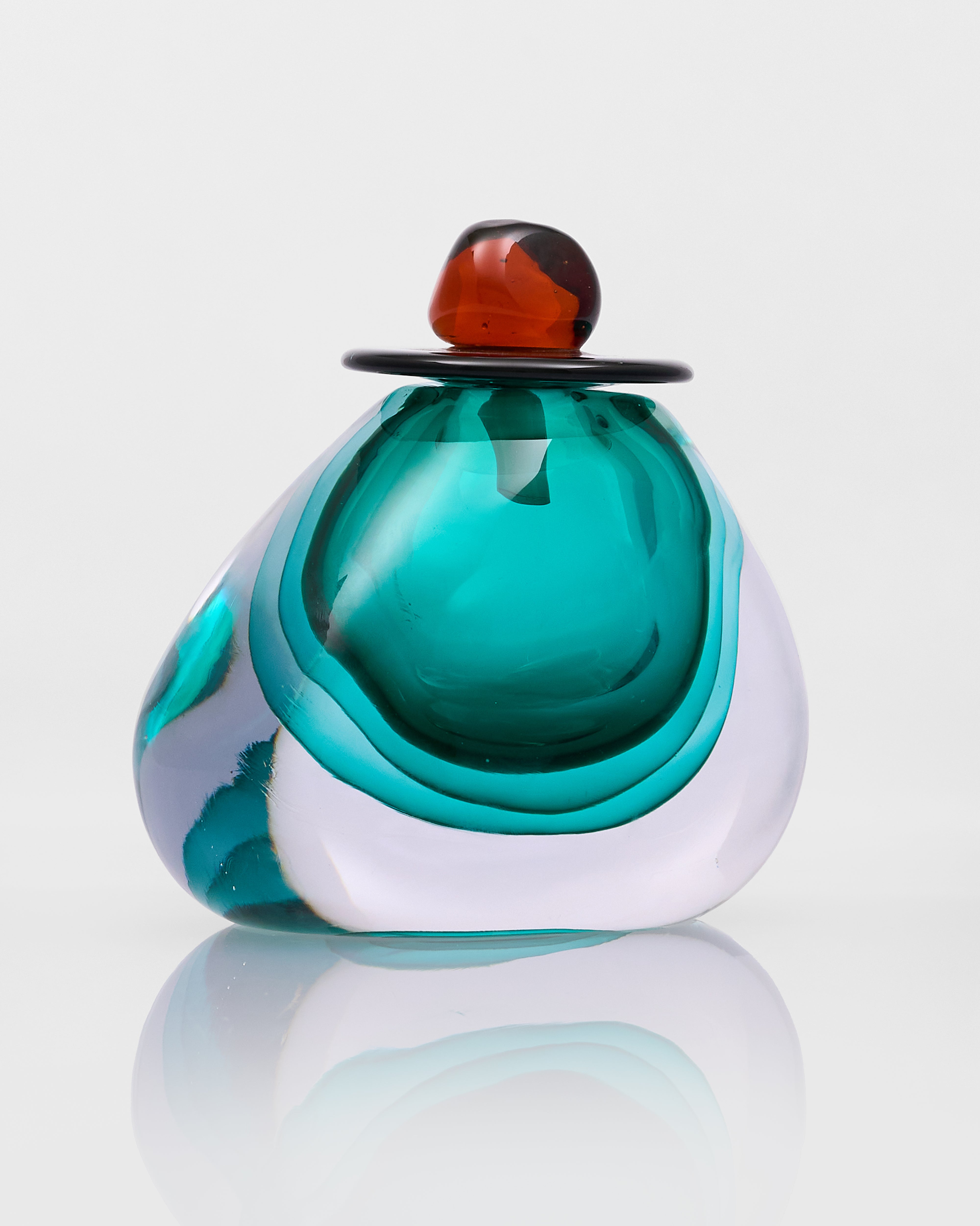 Glass sculpture with teal, white, and amber colors on a reflective surface