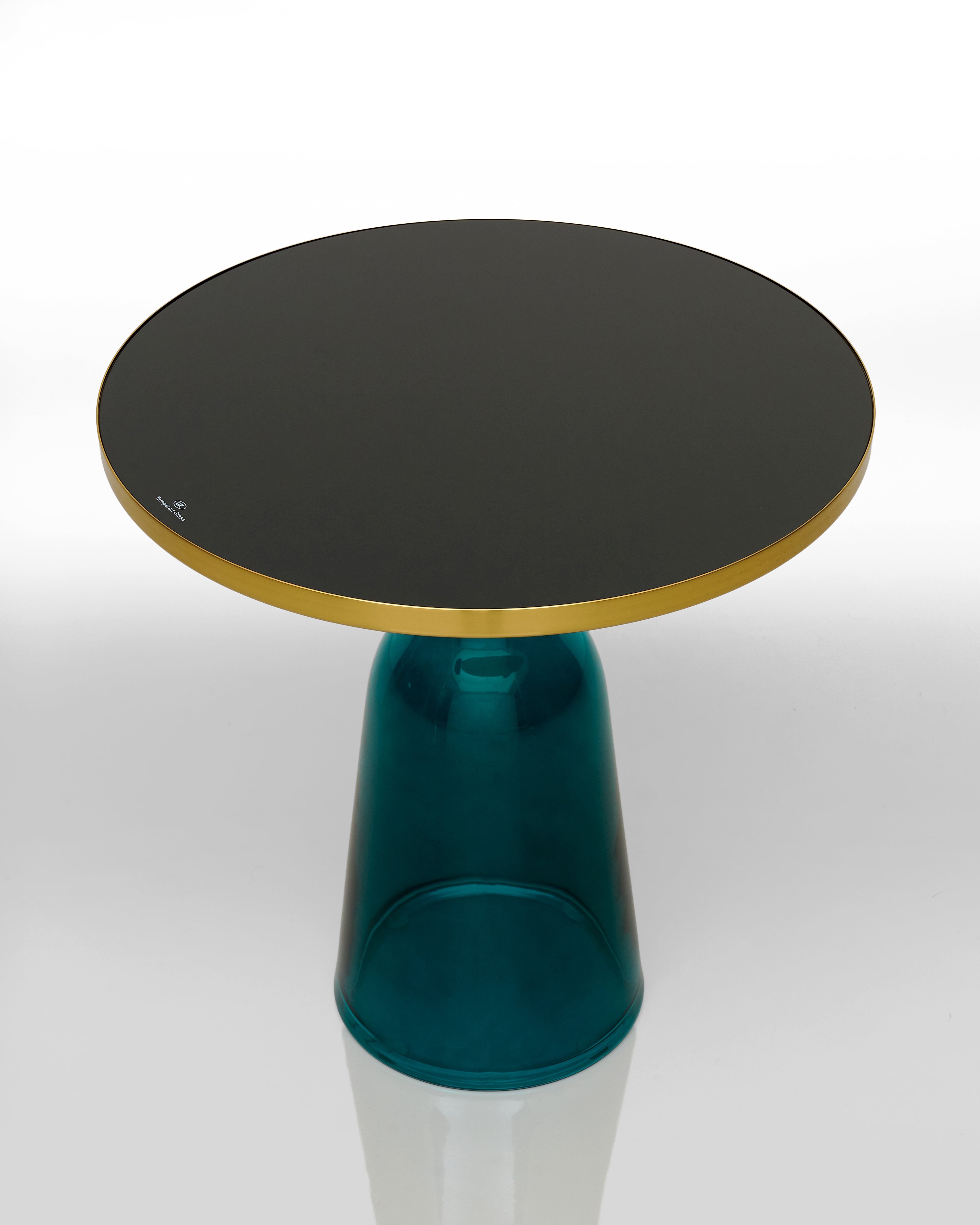 Round black glass table with a teal and gold base on a white background