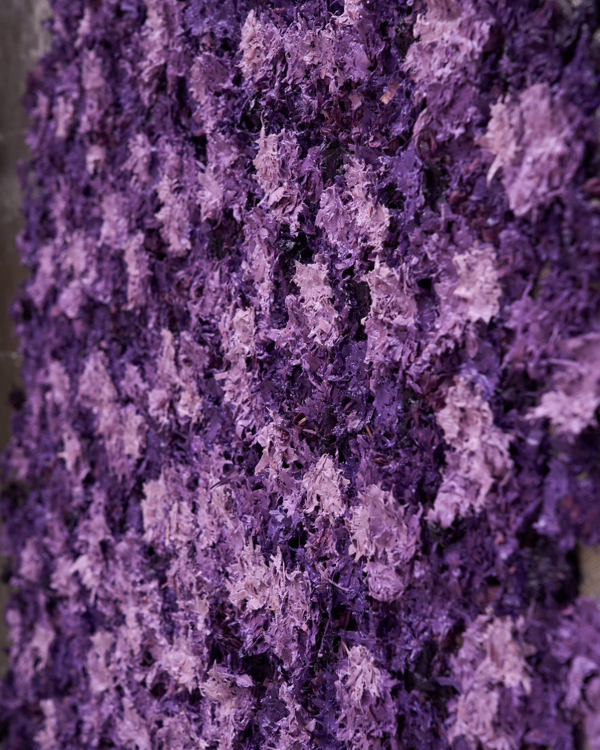 A close-up of a textured purple and lavender floral wall hanging or decorative panel with dense, shaggy flower clusters filling the frame.