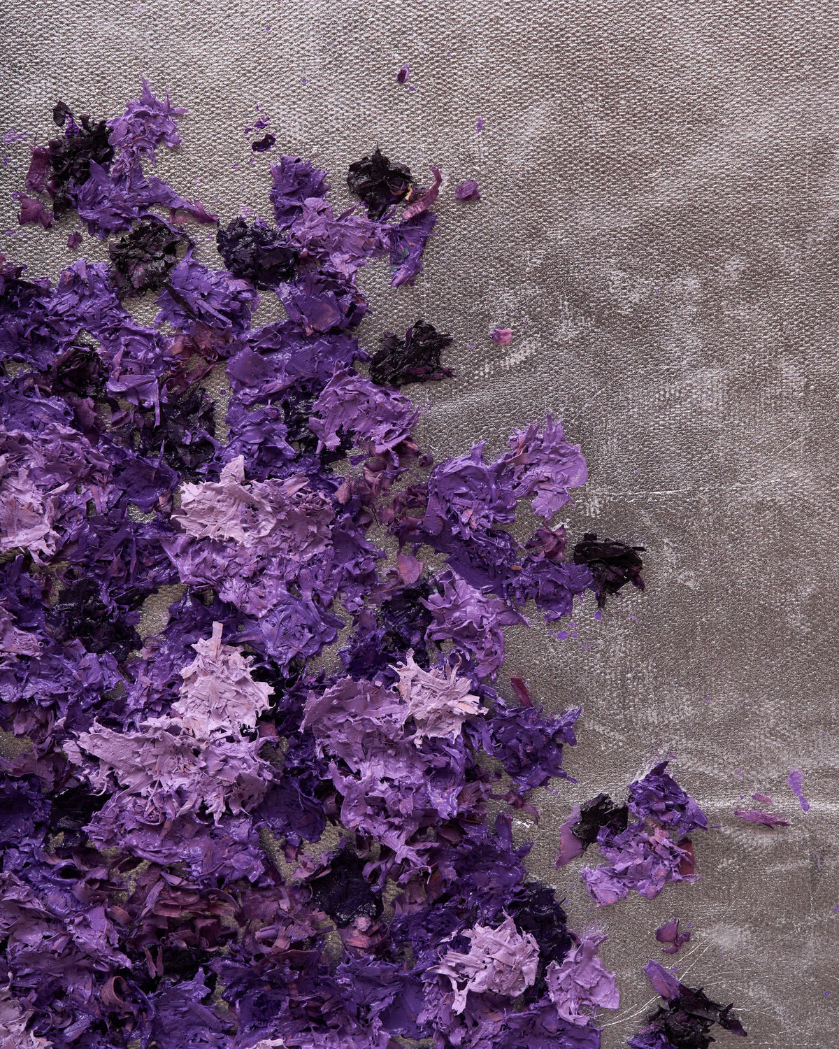 Purple and violet textured paper confetti scattered across a gray fabric background.
