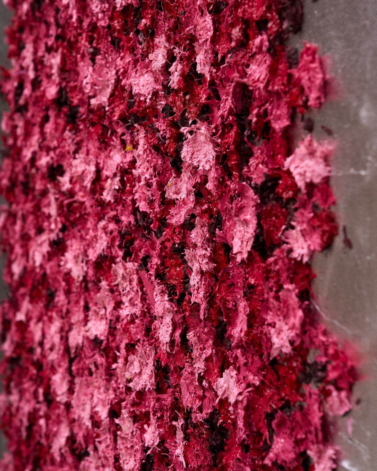 A close-up of textured, shredded decorative material in shades of deep pink, magenta, and burgundy, piled against a neutral gray surface.