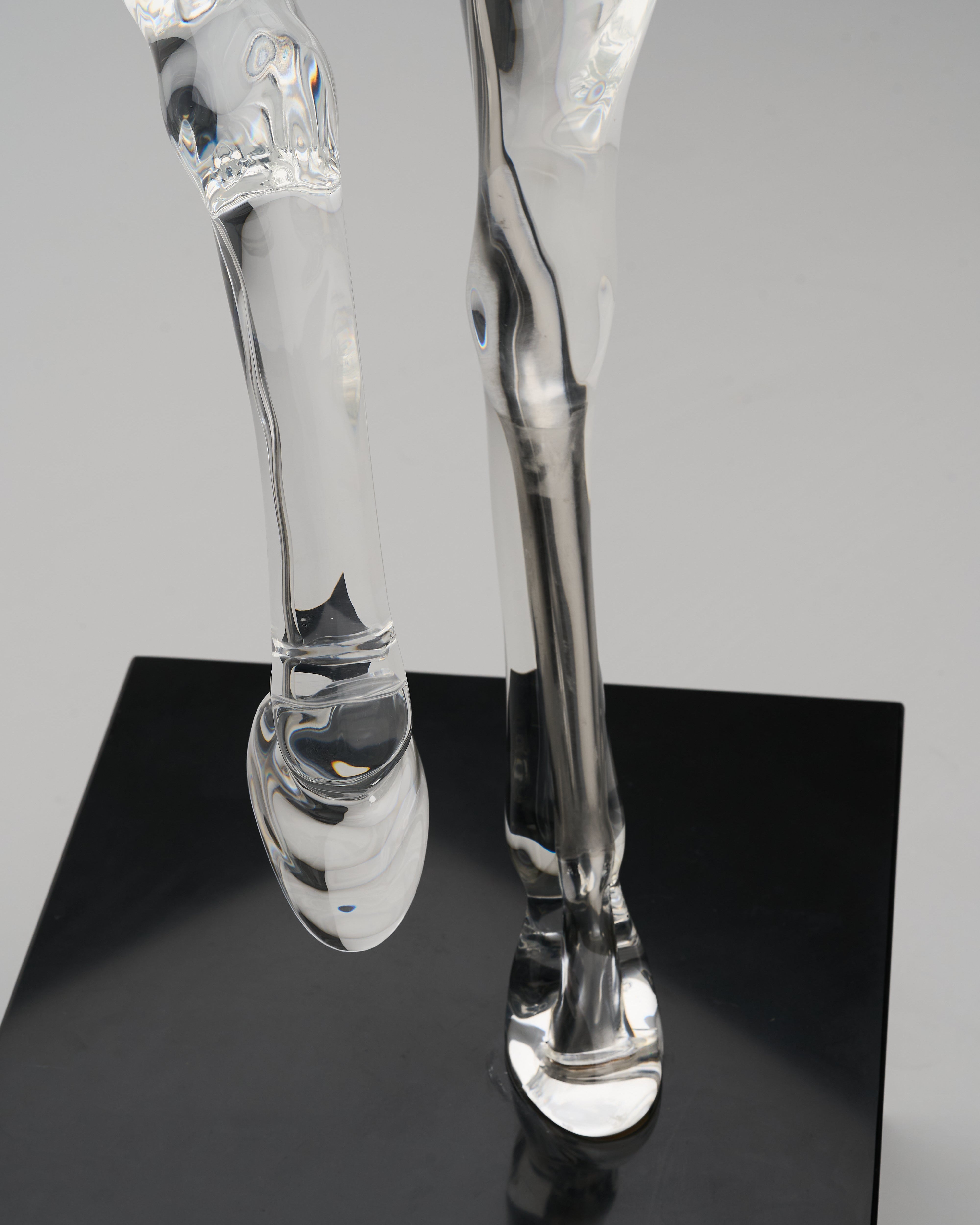 Clear glass sculpture of horse legs on a black platform with a gray background