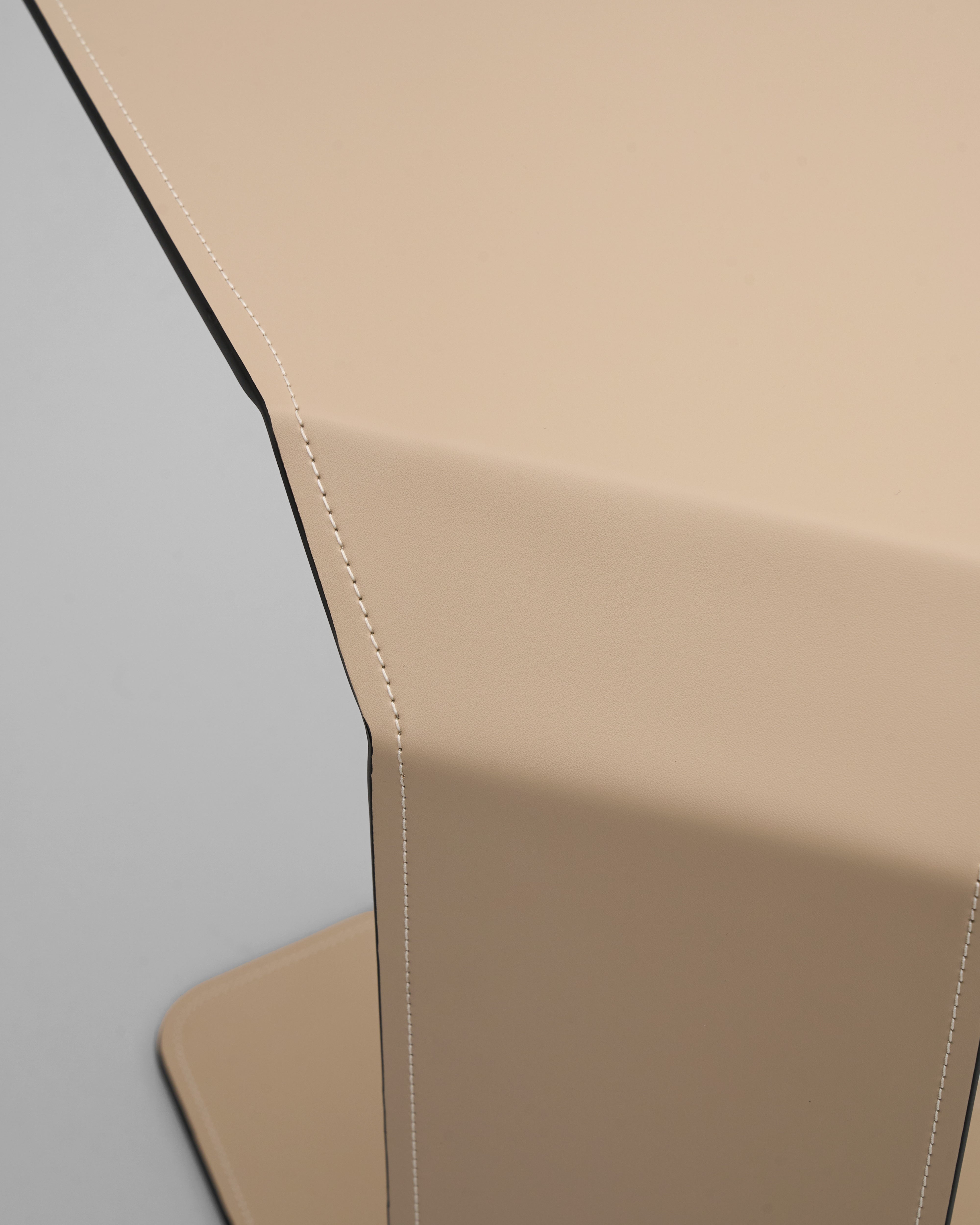 Close-up of beige leather chair with visible stitching on a gray background of the beige side table
