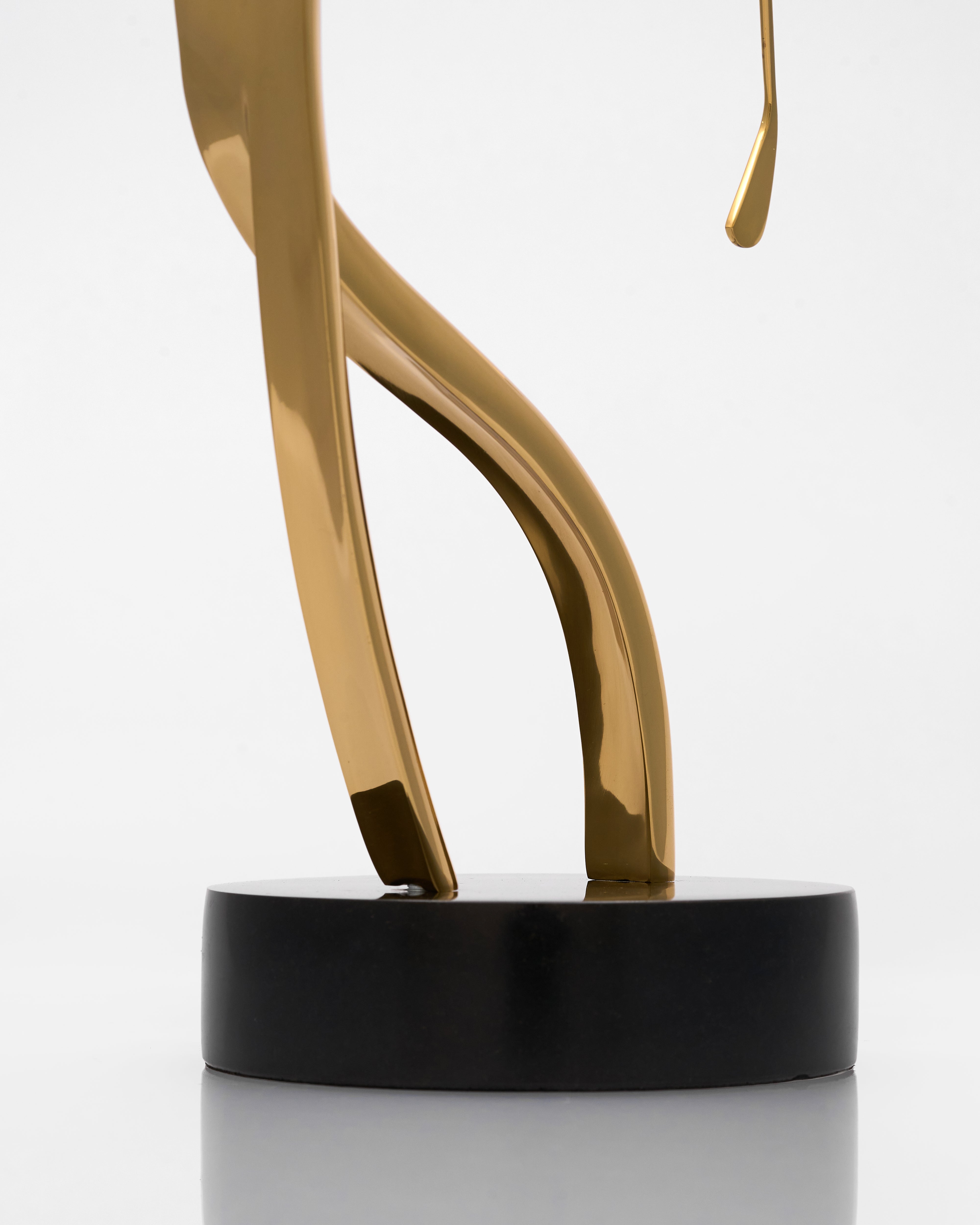 Gold abstract sculpture on a black base against a white background