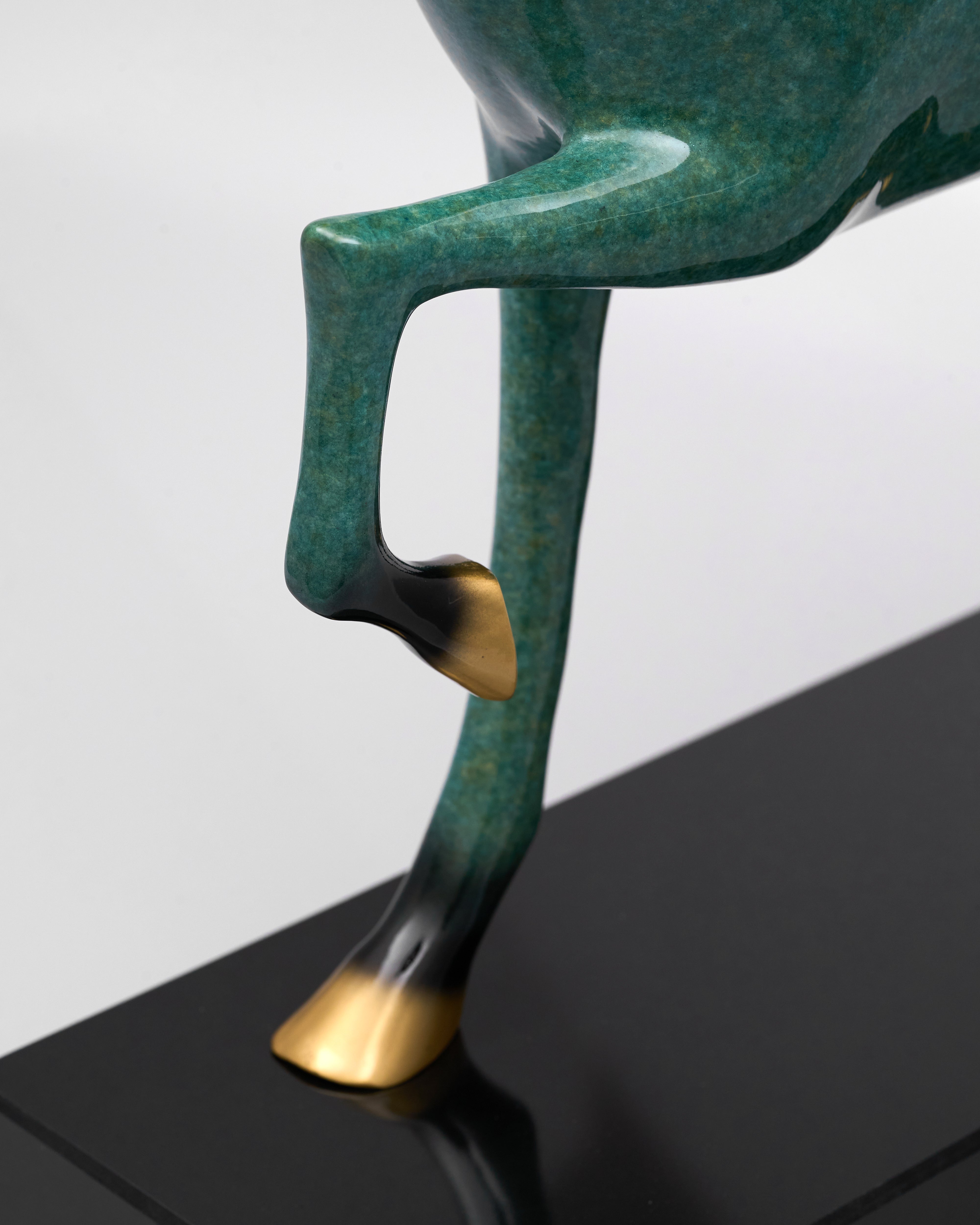 Green and gold sculpture of a figure on a black platform with a white background